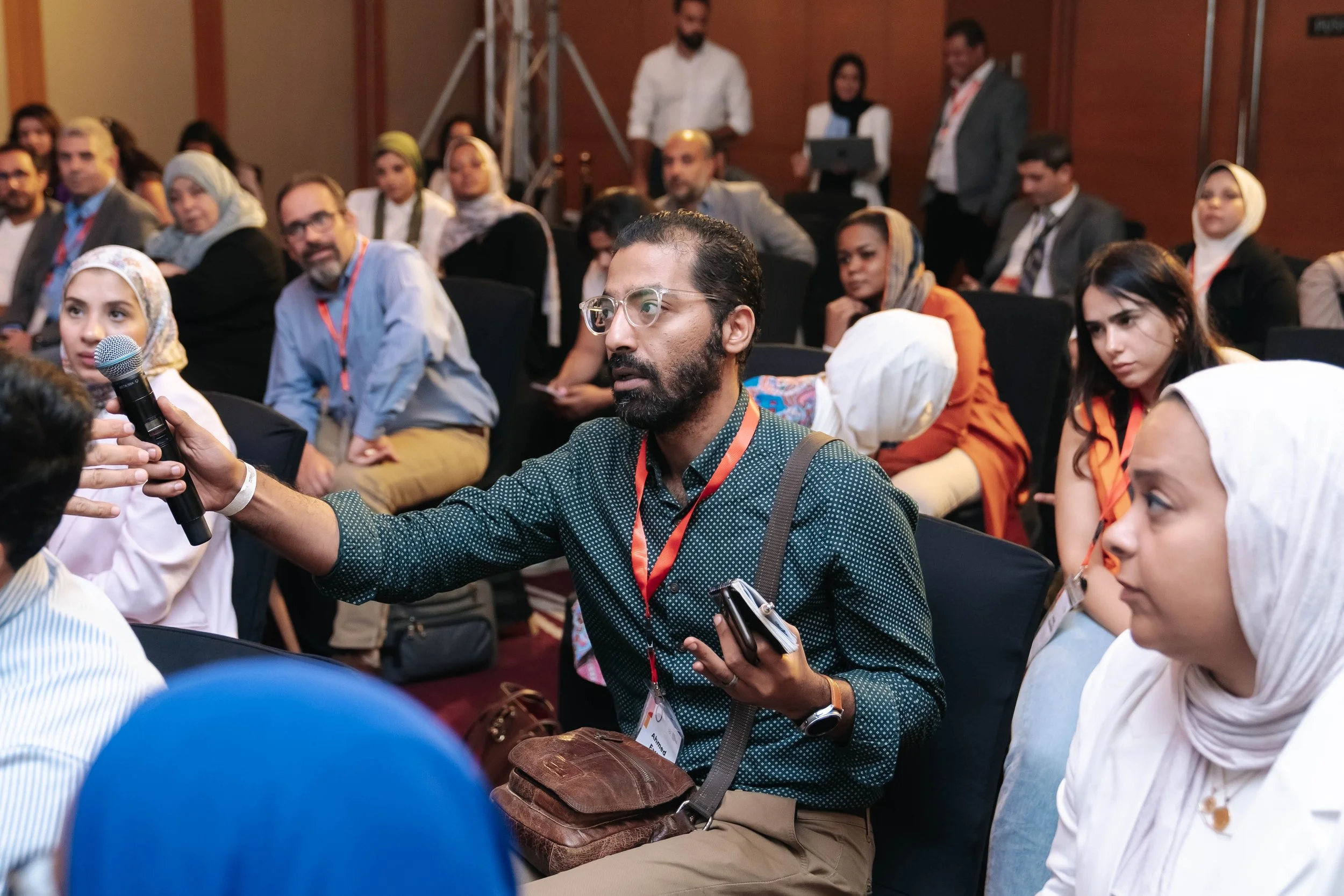 A diverse group of people attending the Regional Sustainable Development Forum, First Edition with one man in the foreground holding a microphone and asking a question.