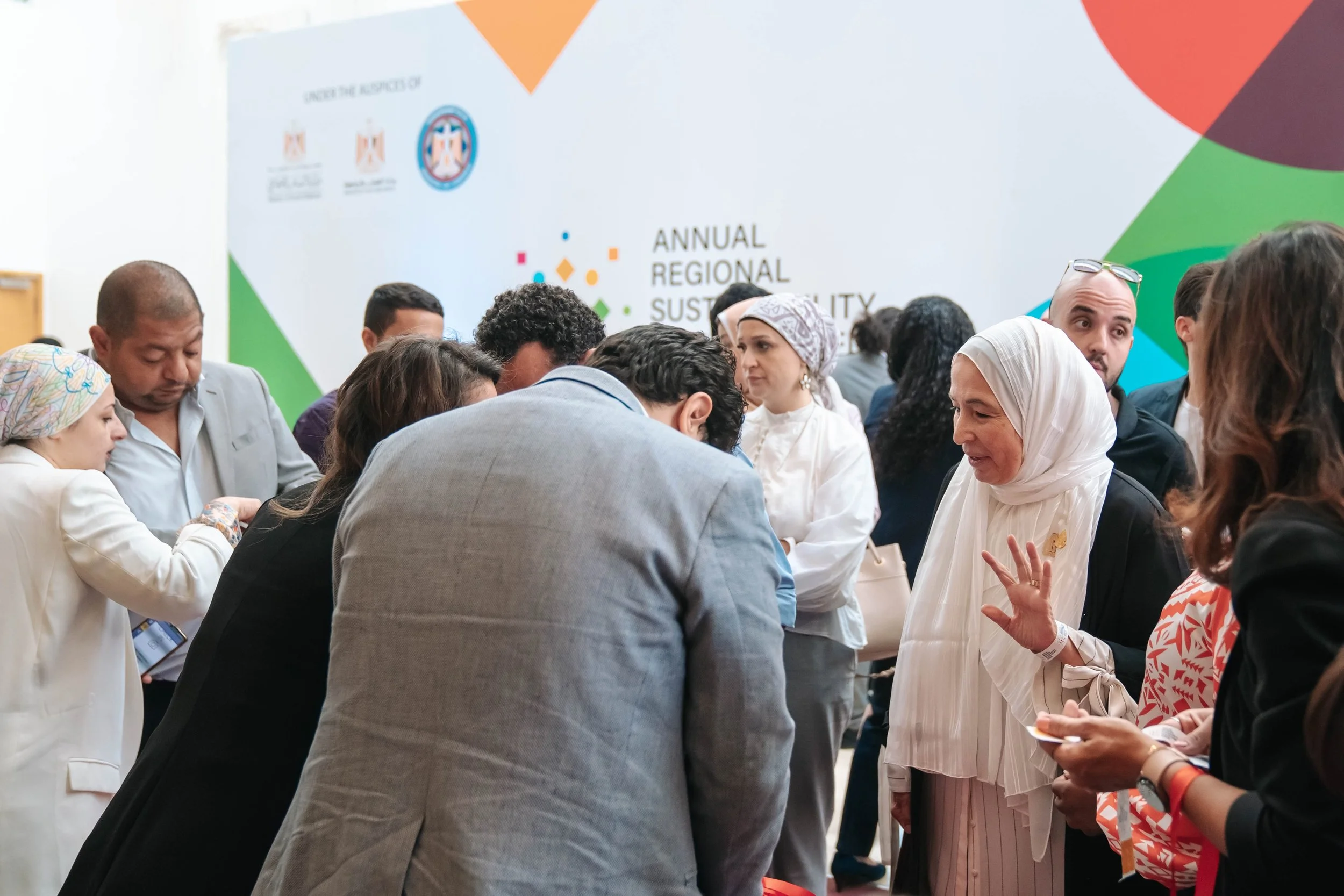 People gathered at the Regional Sustainable Development Forum, First Edition, engaging in conversations, with a banner in the background that reads 'Annual Regional Sustainability' and logos of organizations and governments.