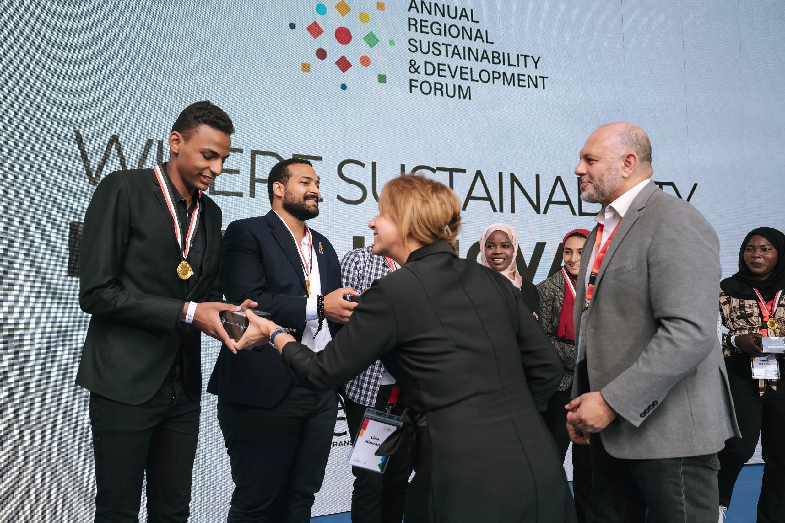 A group of people at an awards ceremony during the Regional Sustainable Development Forum, First Edition. One man receives a medal from the organizers, with several others smiling and observing.