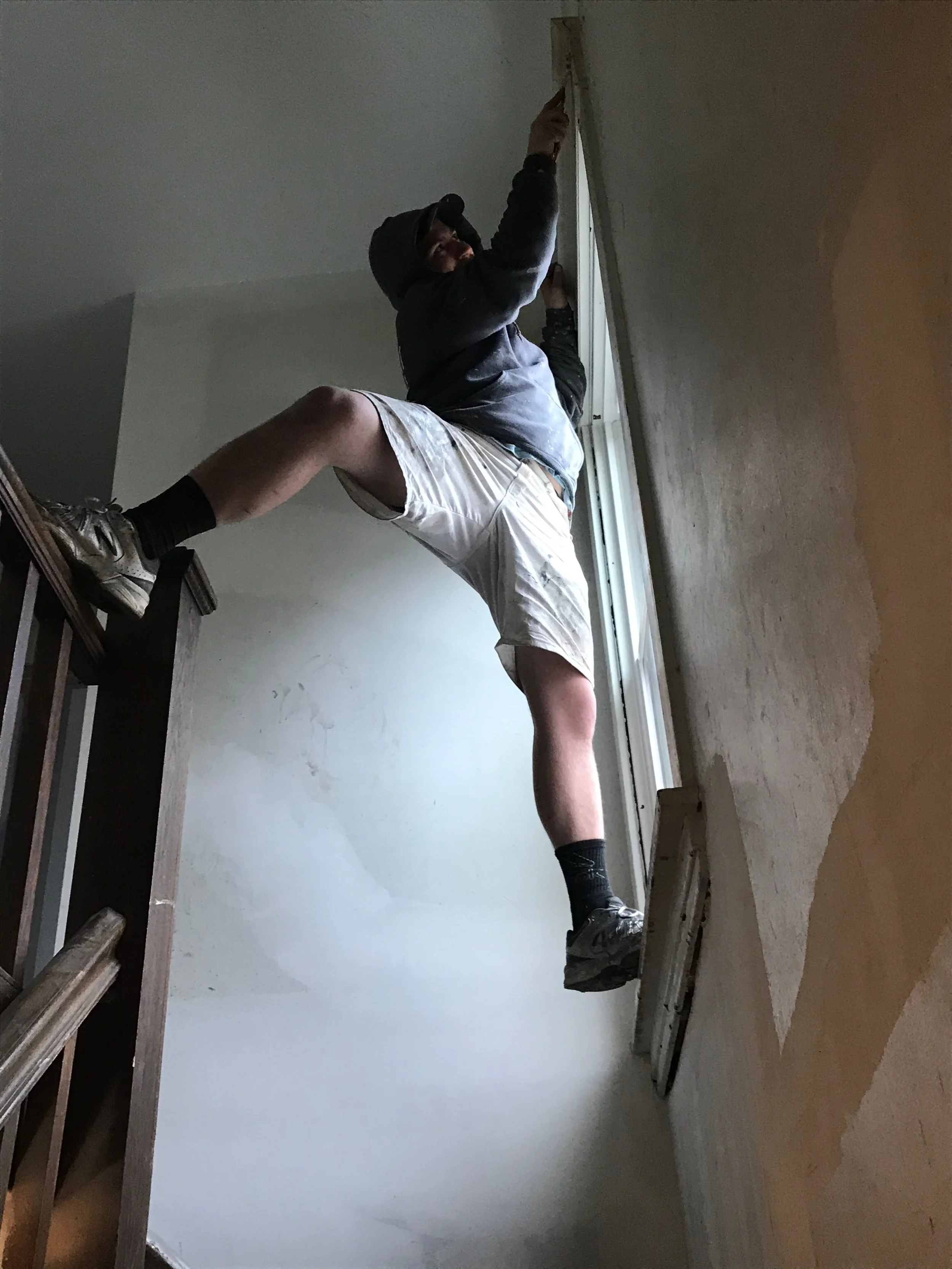 A person standing on a ladder, using a tool near the ceiling in a room undergoing renovation or repair.