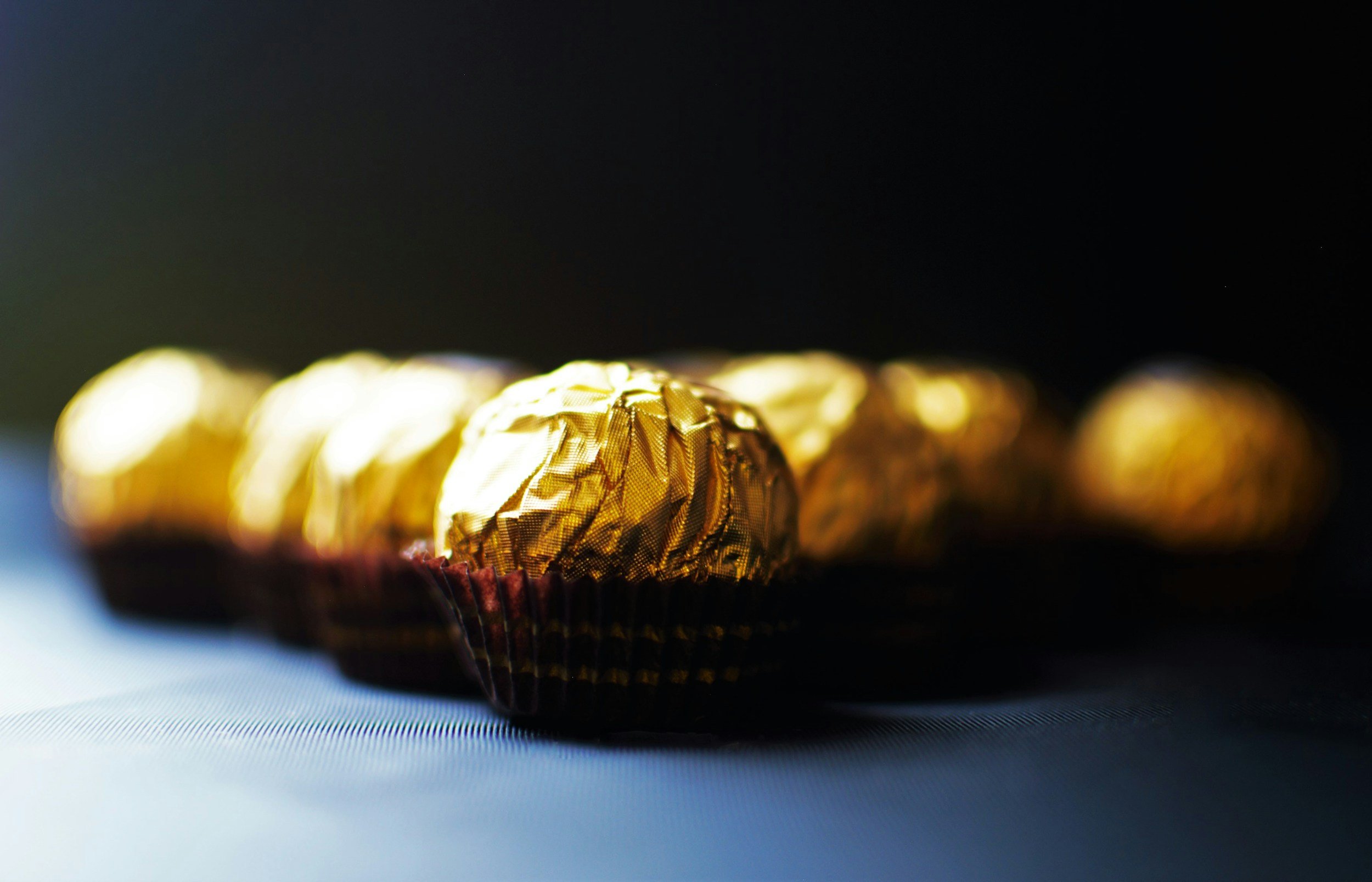 Close-up of Ferrero Rocher chocolates wrapped in gold foil, arranged in a row on a dark surface.