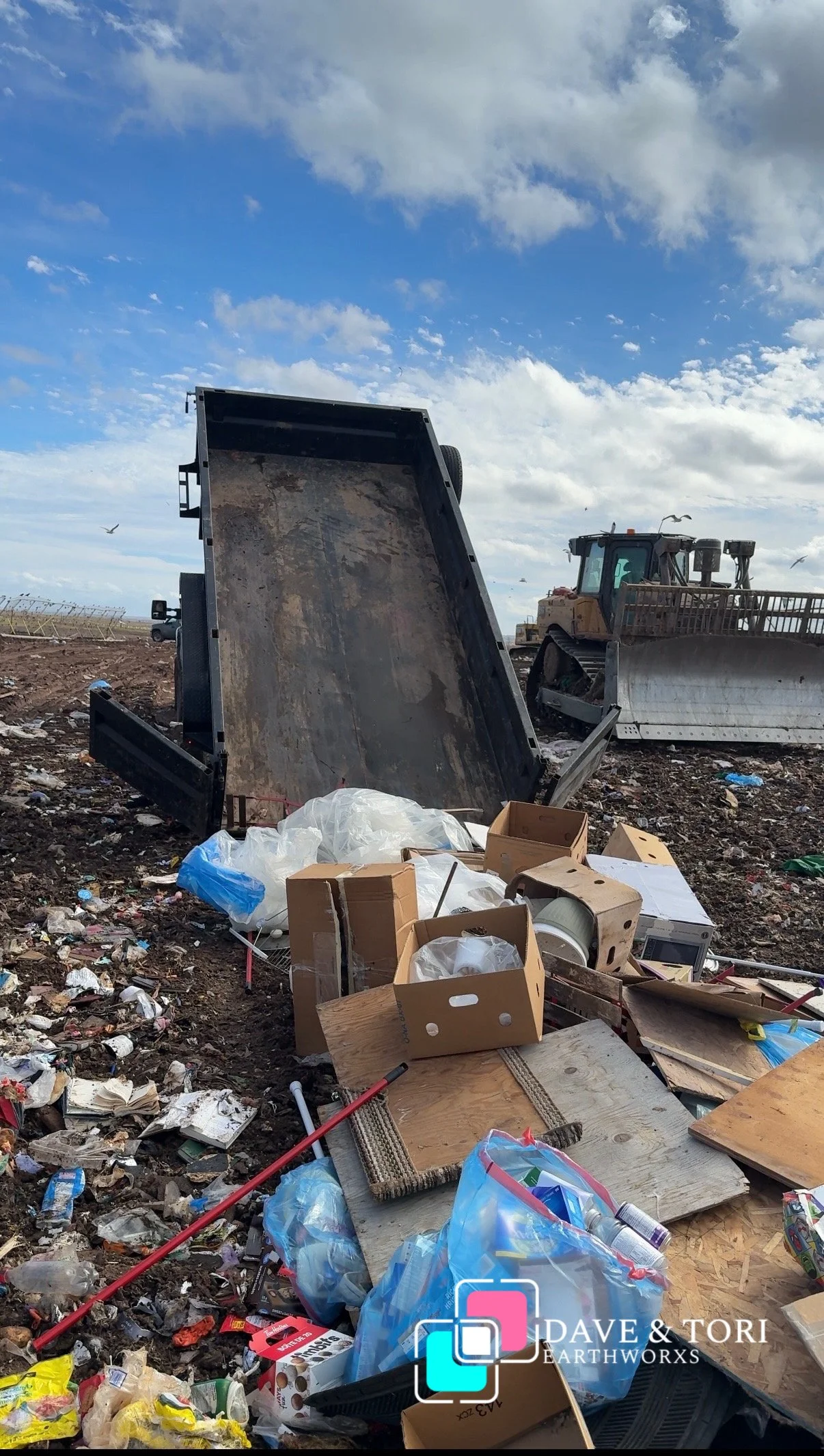 Open trash bin with scattered trash and debris, construction machinery in the background under a partly cloudy sky.