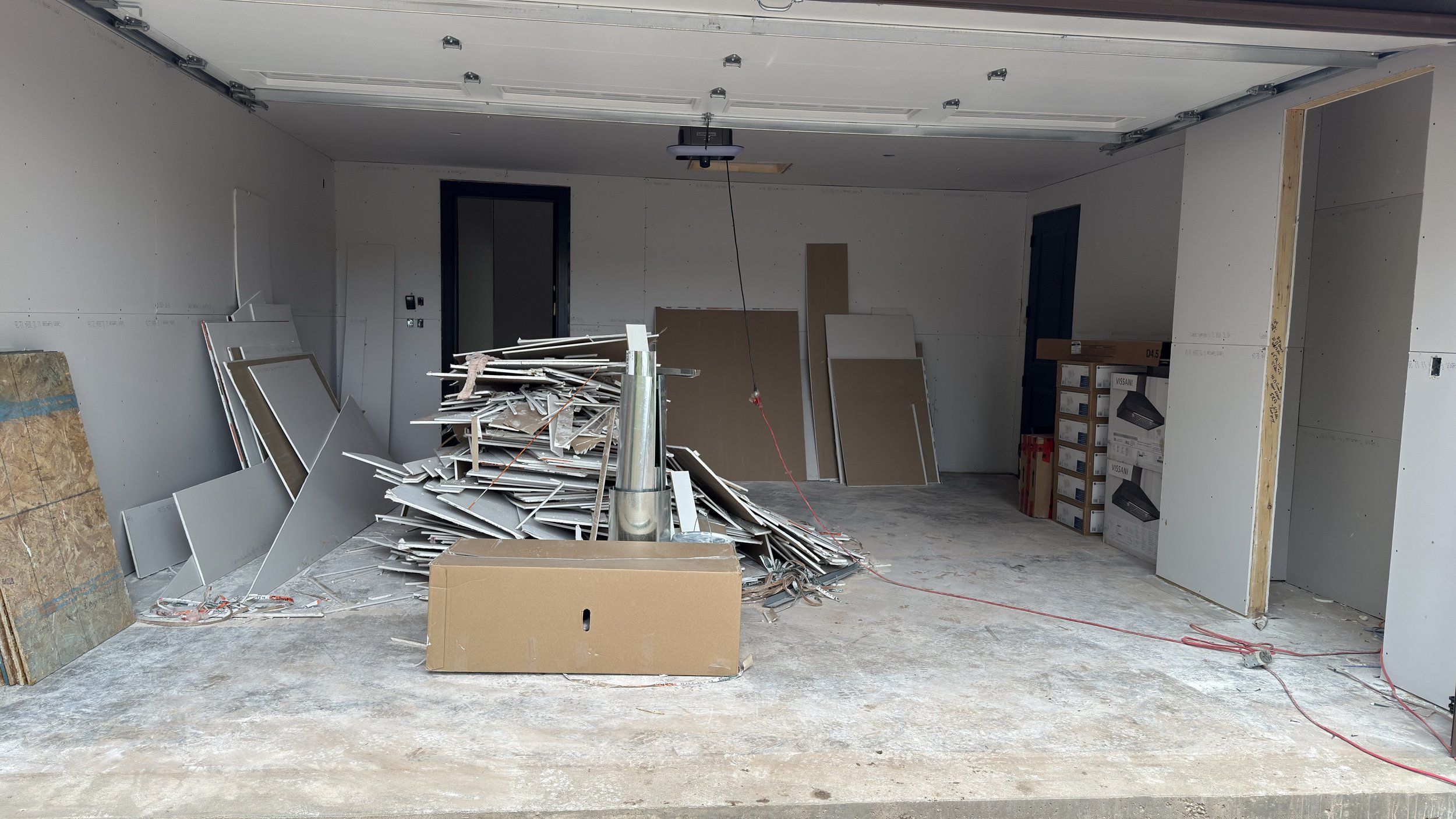 An unfinished garage with construction materials, drywall, and boxes inside.