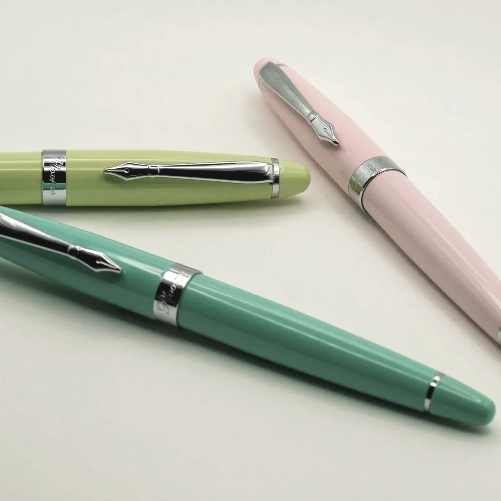 Three pastel-colored fountain pens in green, pink, and turquoise on a white surface.