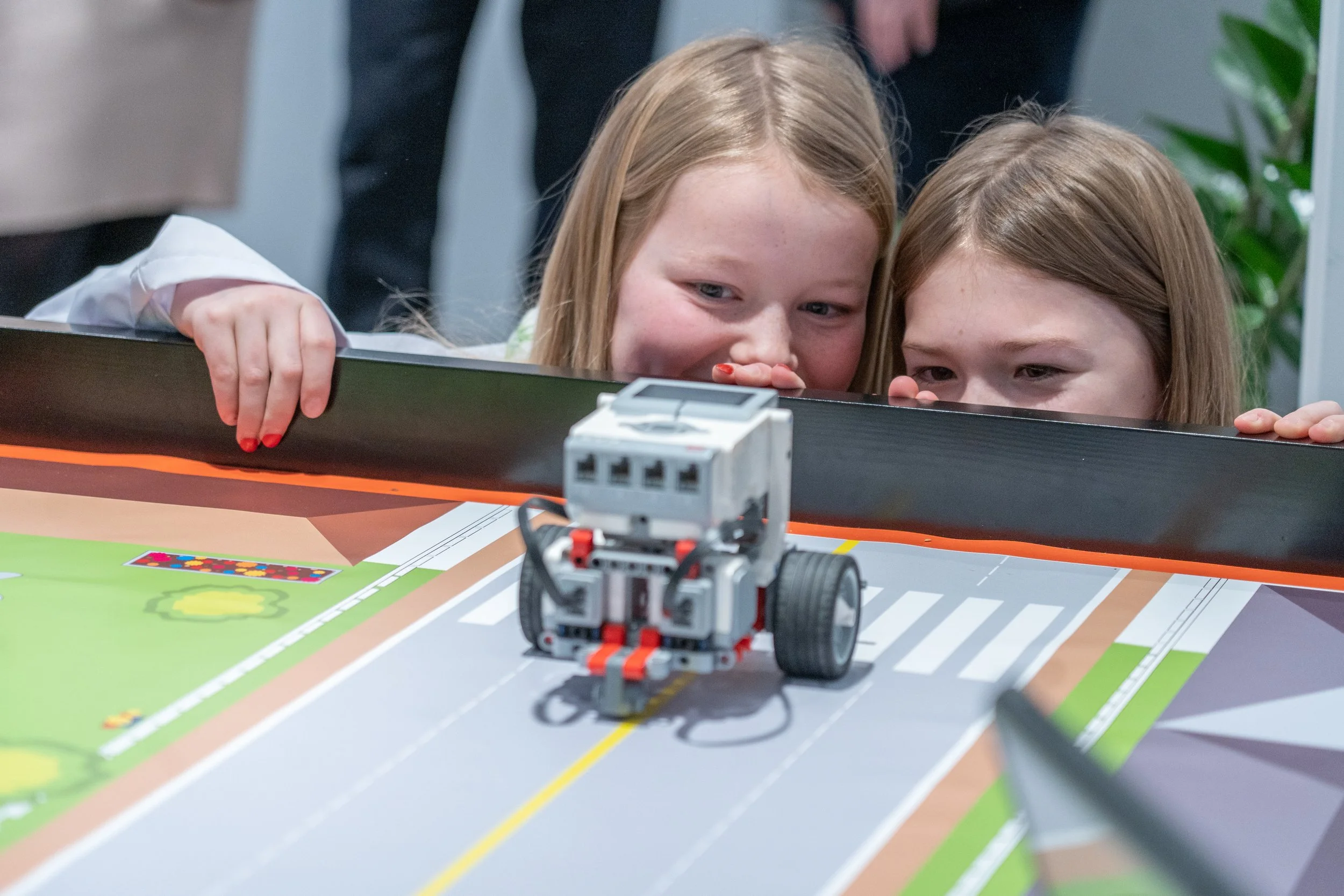 To unge jenter som ser på en liten robot på et spillbord.