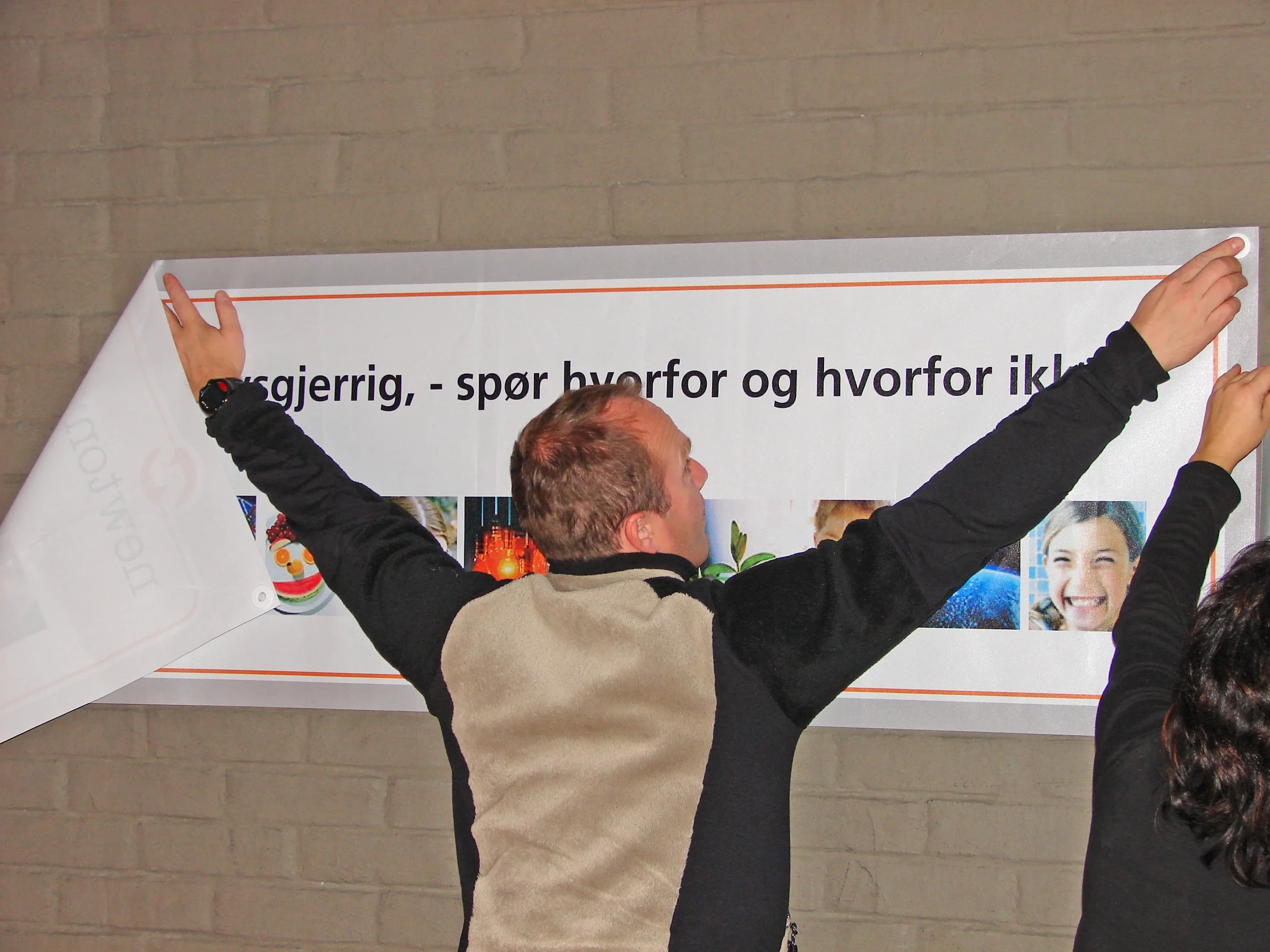 To personer henger opp en stor plakat på en vegg.