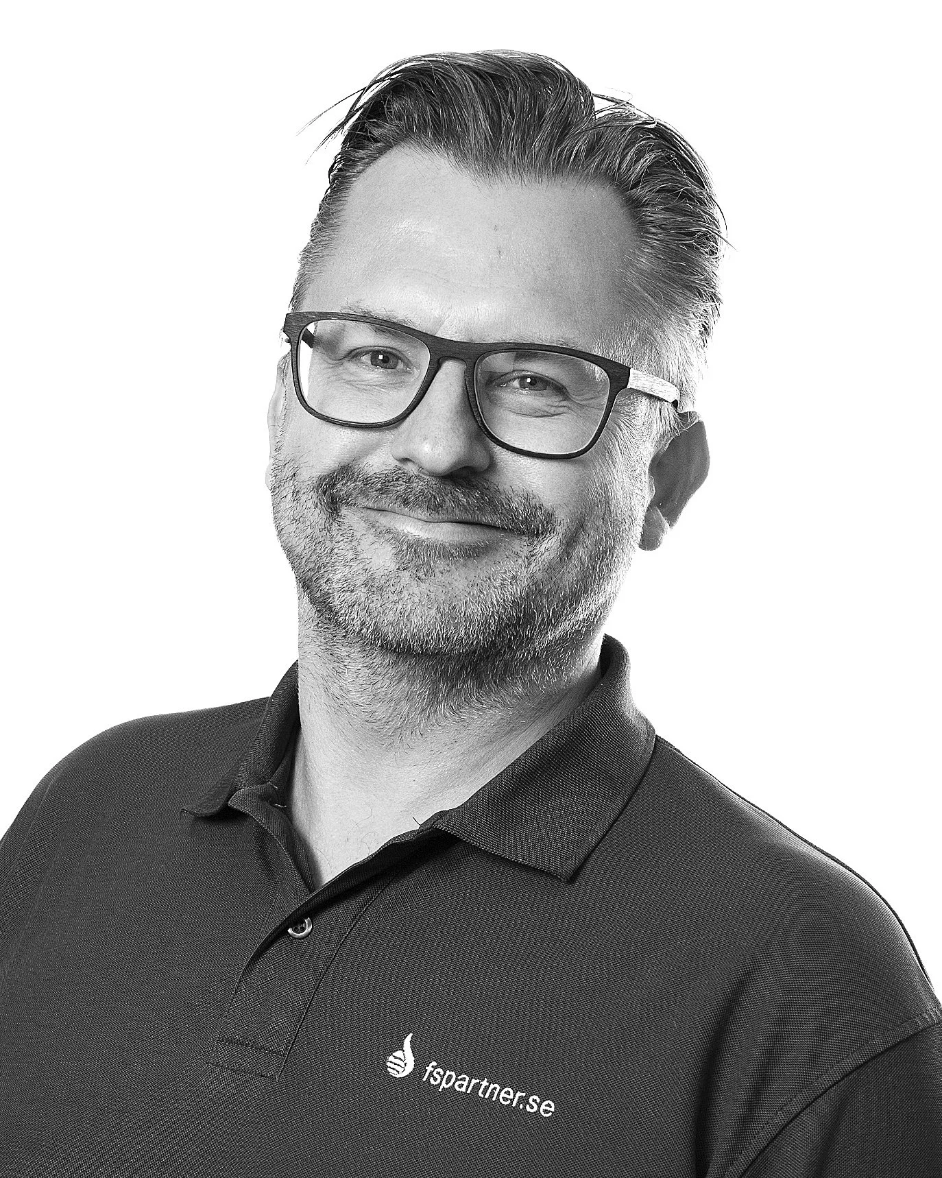 En mann med brunt grått hår og skjegg, iført briller og svart polo med logoen "fspartner.se" står foran en lys bakgrunn.