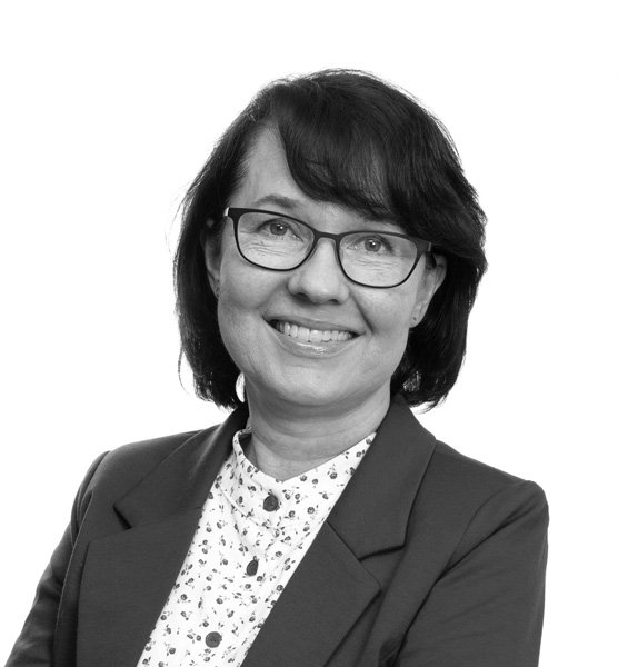 Portrett av en kvinne med briller, smilende, i formell påkledning, mot en hvit bakgrunn.