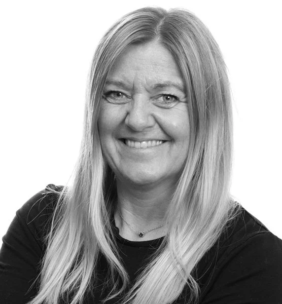 Portrett av en kvinne med lang blond hår, smilende, svart klær, mot en hvit bakgrunn.