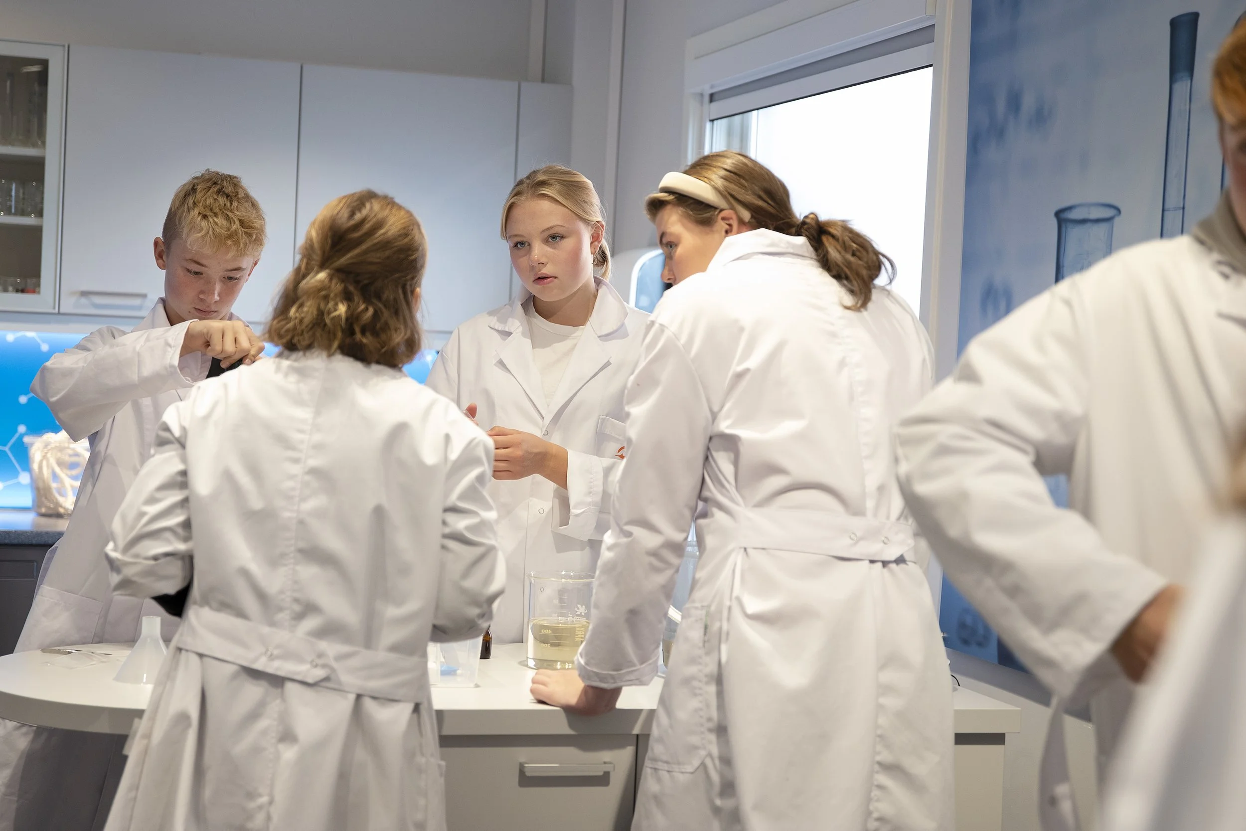 Gruppemedlemmer i hvite laboratoriefrakker som utfører eksperimenter i et moderne laboratoriemiljø.