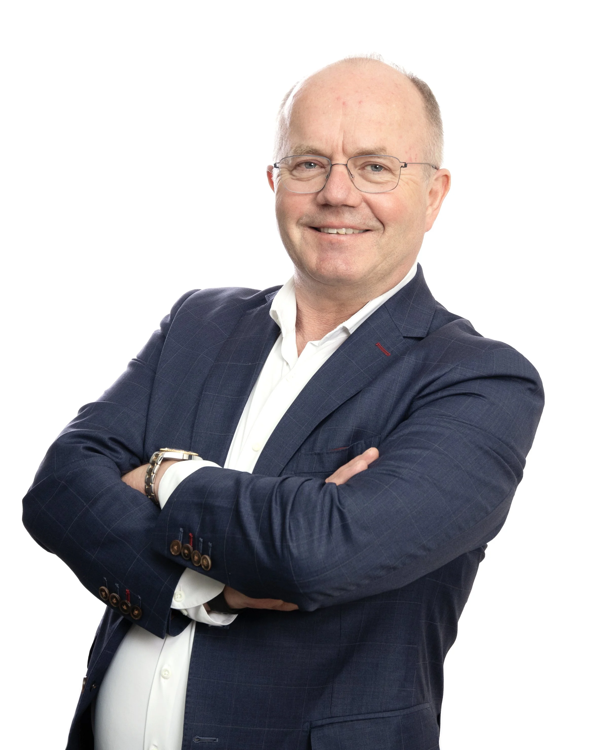 En mann med blå øyne, briller, smilende med armene over brystet, iført mørk blå dress og hvit skjorte, ser direkte på kamera.