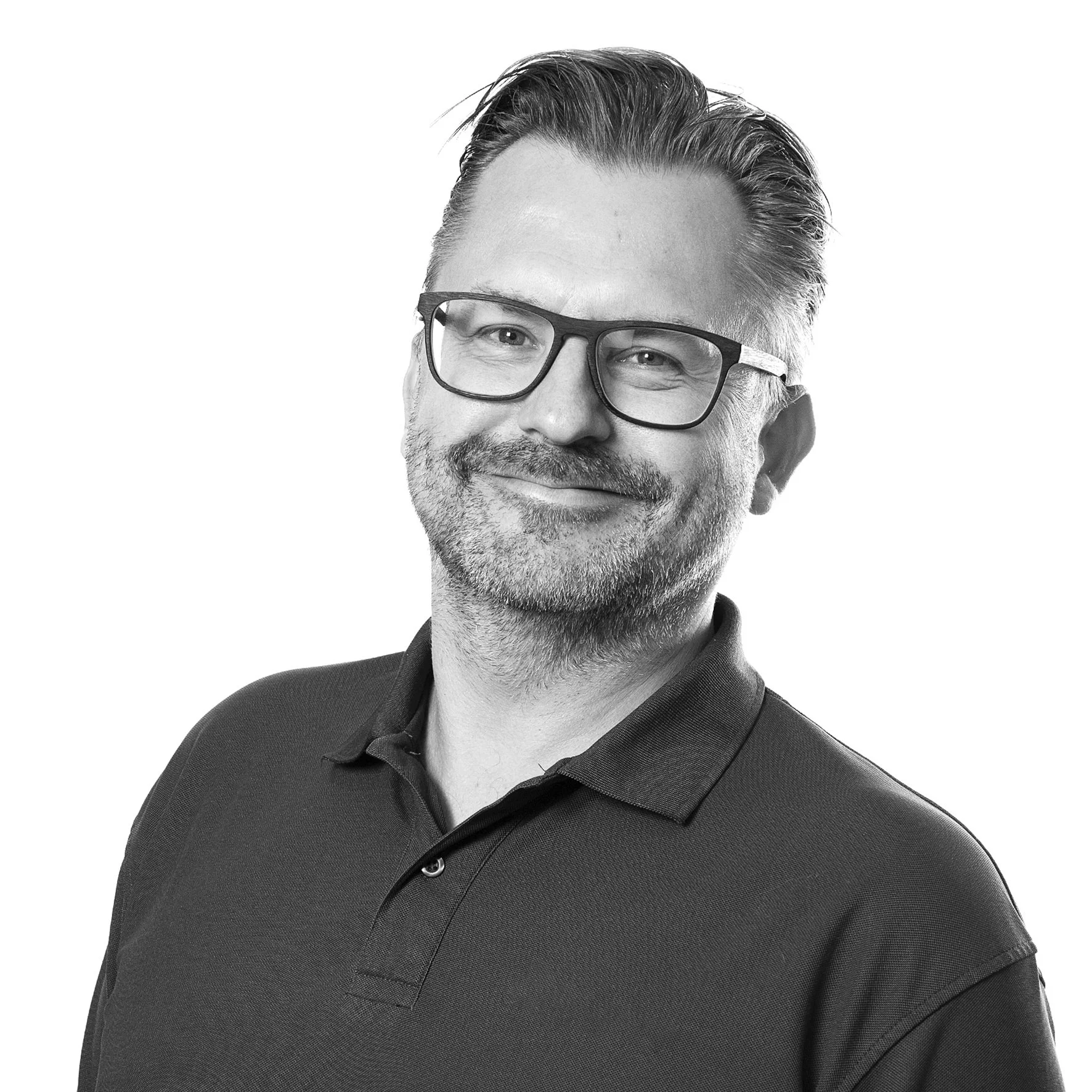 Portrett av en mann med brunt hår, skjegg og briller, iført svart skjorte, smilende.