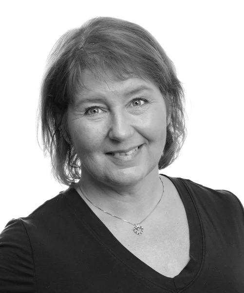 Portrett av en voksen kvinne med kort, grått hår, smilende, iført svart topp og smykkekjede