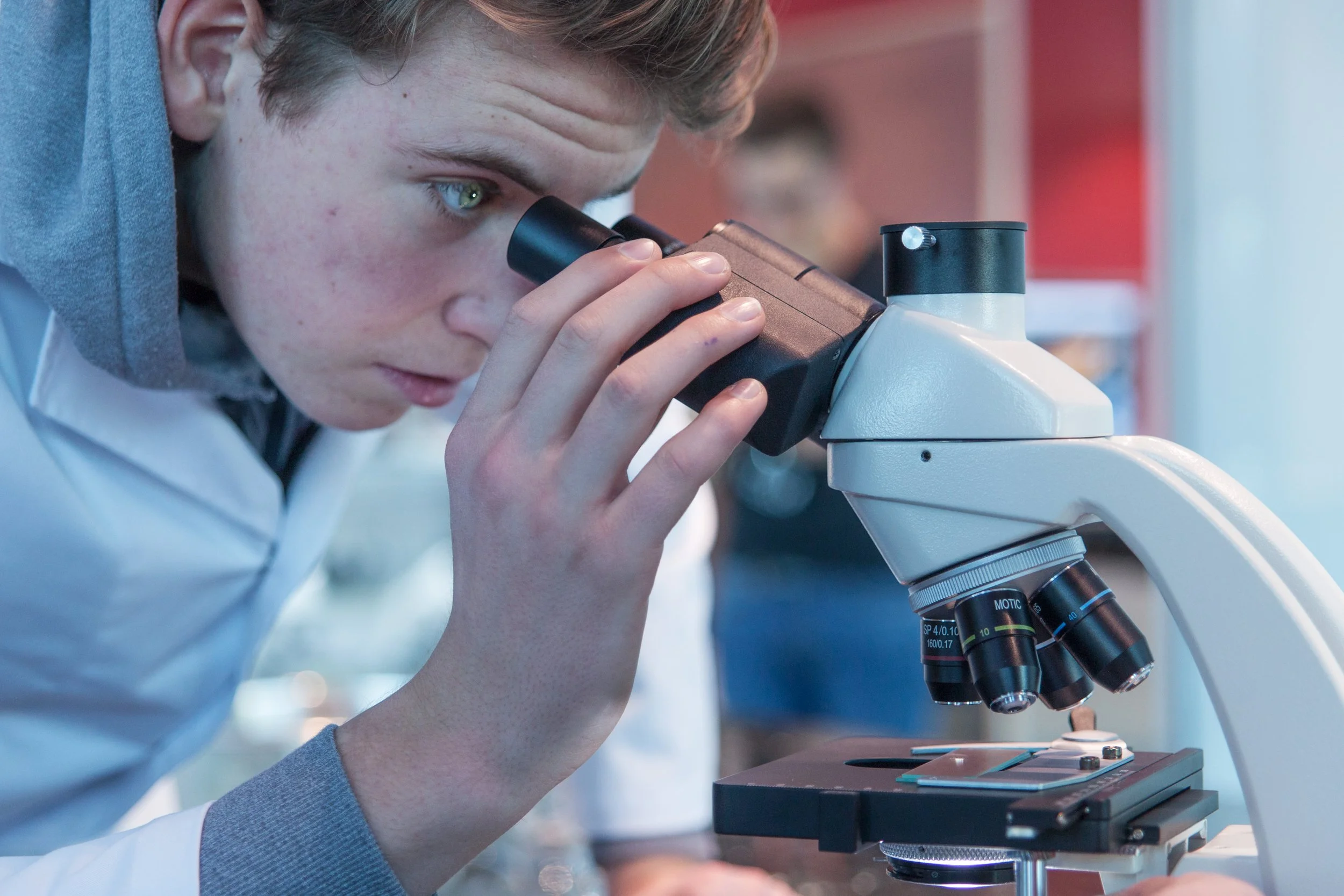 En ung mann i hvit labfrakk ser gjennom en mikroskop i et laboratorie.