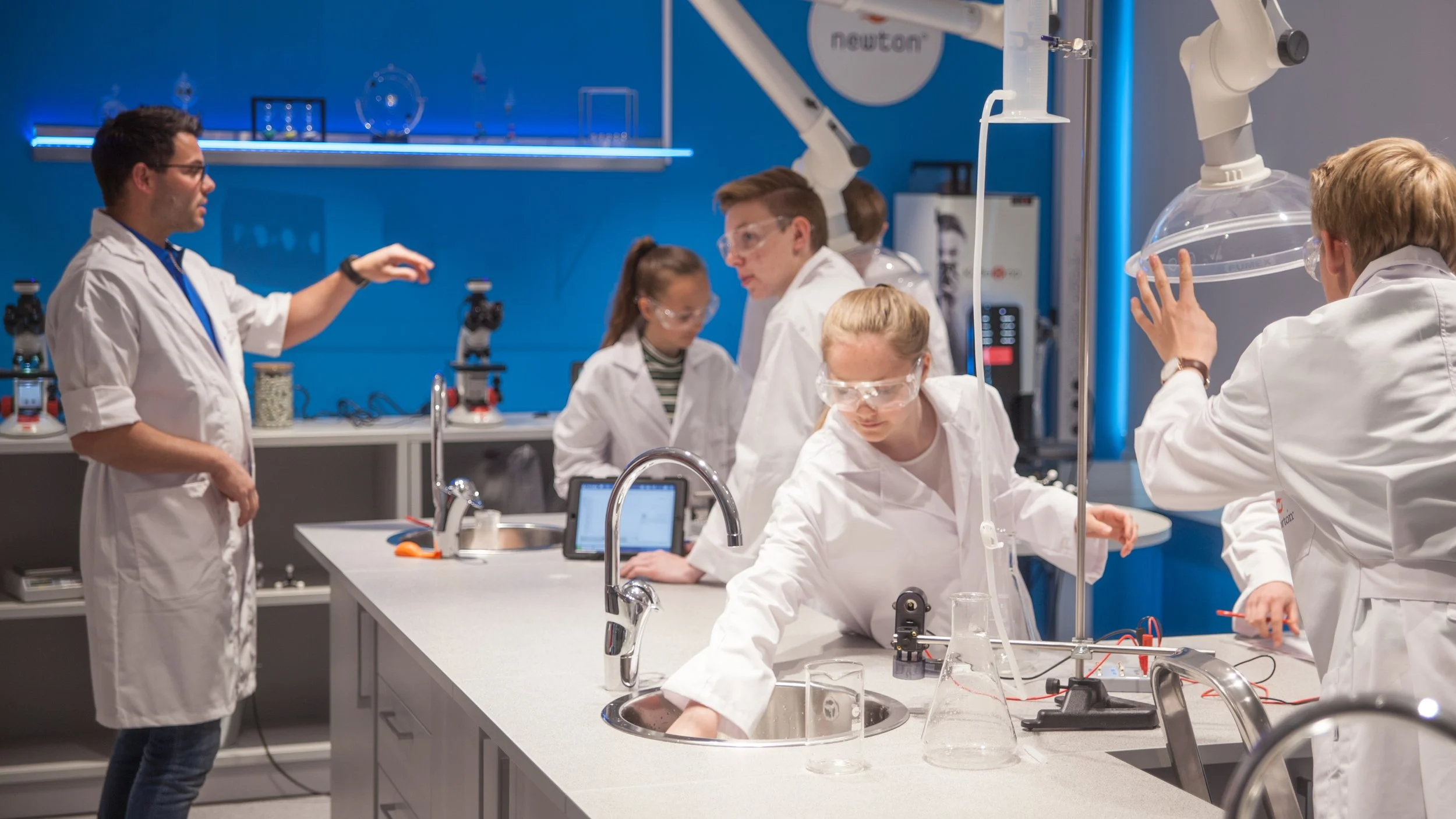 Gruppe unge forskere i laboratoriet, bruker vernebriller og labjakker, jobber med forskning og eksperimenter.