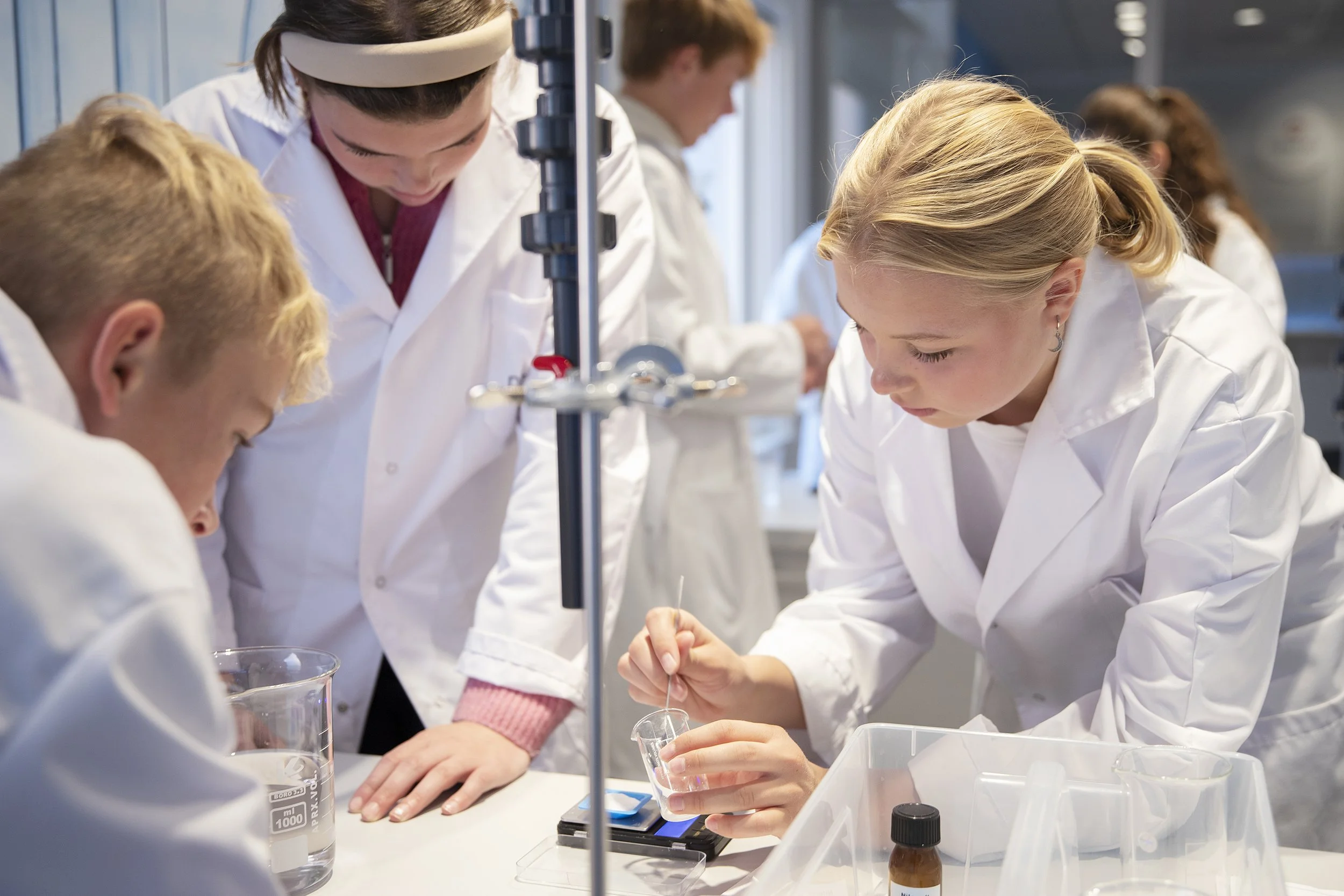 Gruppemedlemmer i hvite labåker utfører eksperimenter i et laboratorie.