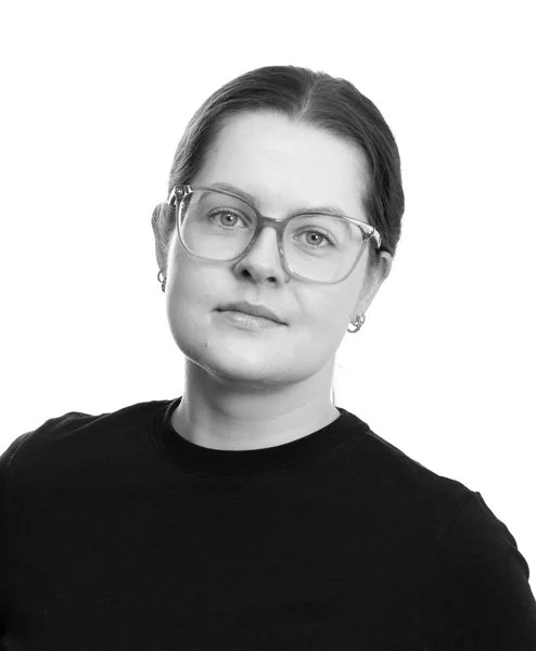 Portrett av en kvinne med briller og kort hår, svart genser, på hvit bakgrunn.