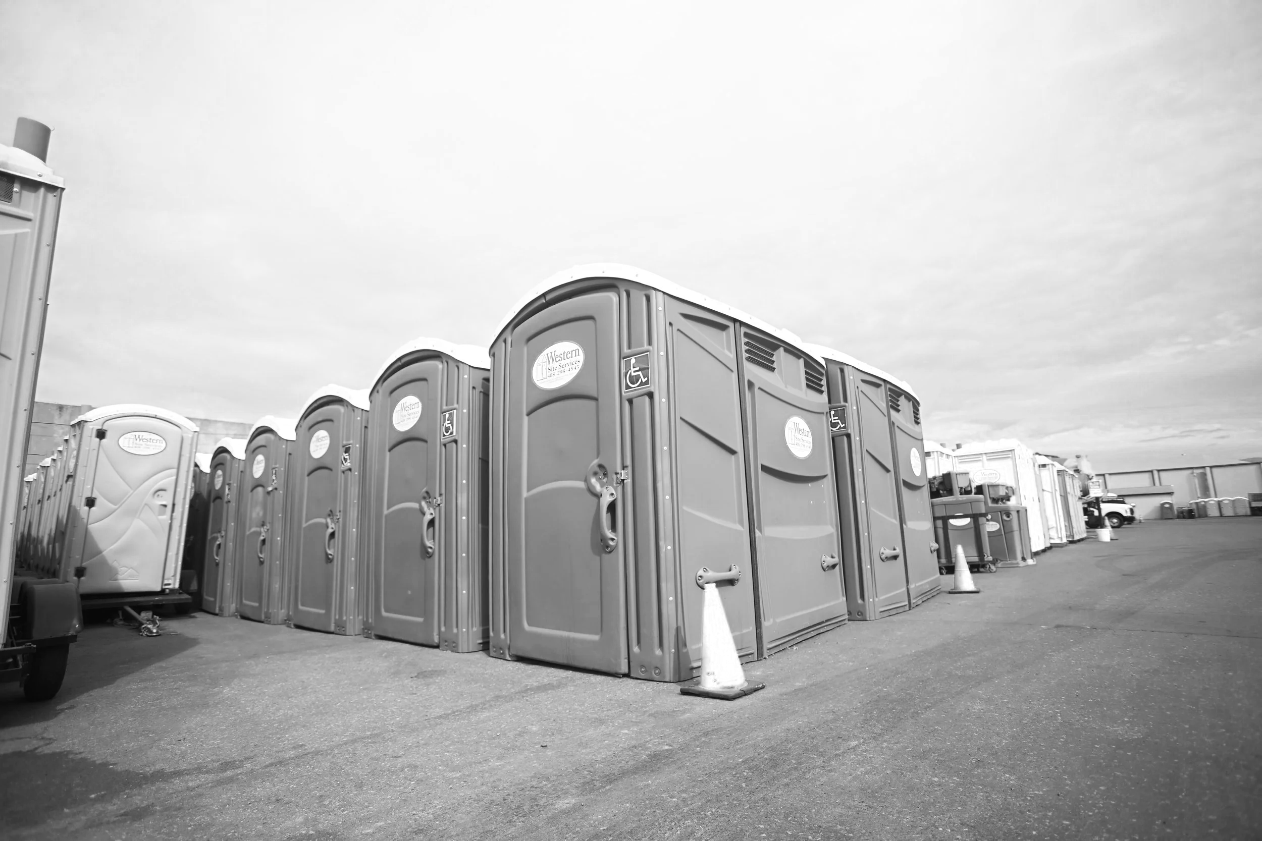 A row of portable toilets with a handicap accessibility sign, set up in an open area under a cloudy sky.