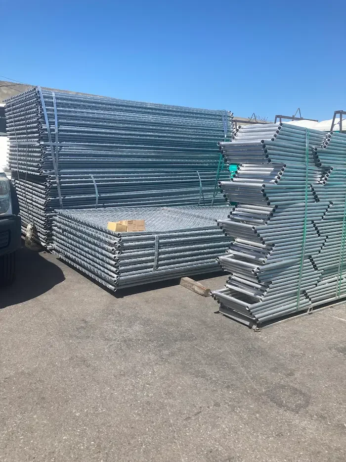 Stacks of metallic scaffolding pipes and platforms outdoors on a paved surface with a clear blue sky.