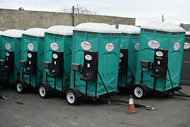 Row of teal portable toilets parked outdoors with a construction cone in front.