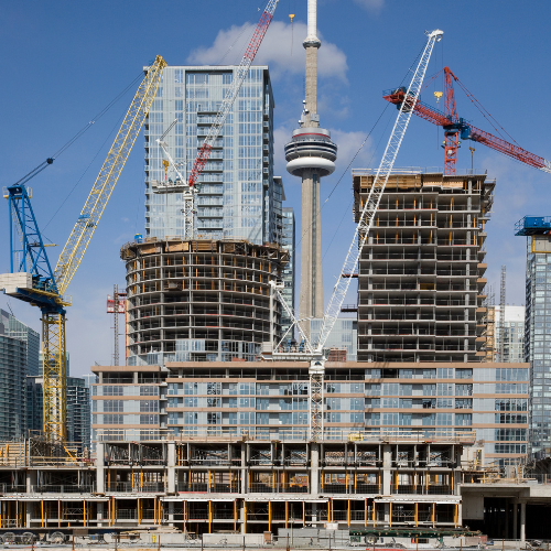 Construction site with multiple cranes and partially built high-rise buildings in Toronto, with CN Tower in the background.