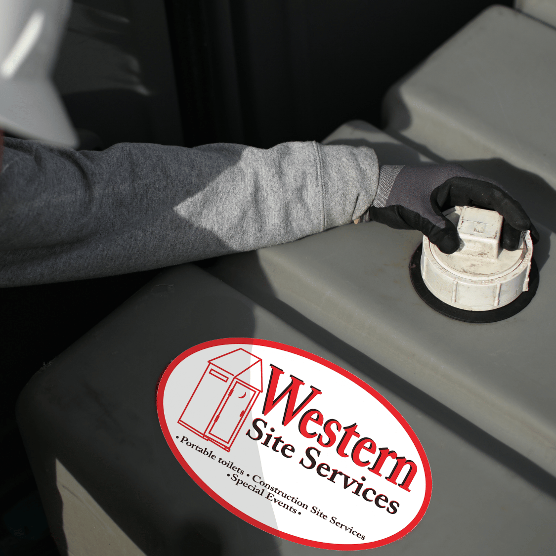 A person wearing a gray long sleeve shirt and a black glove operating a portable toilet valve or lid on a tank, with a Western Site Services sticker on the tank.