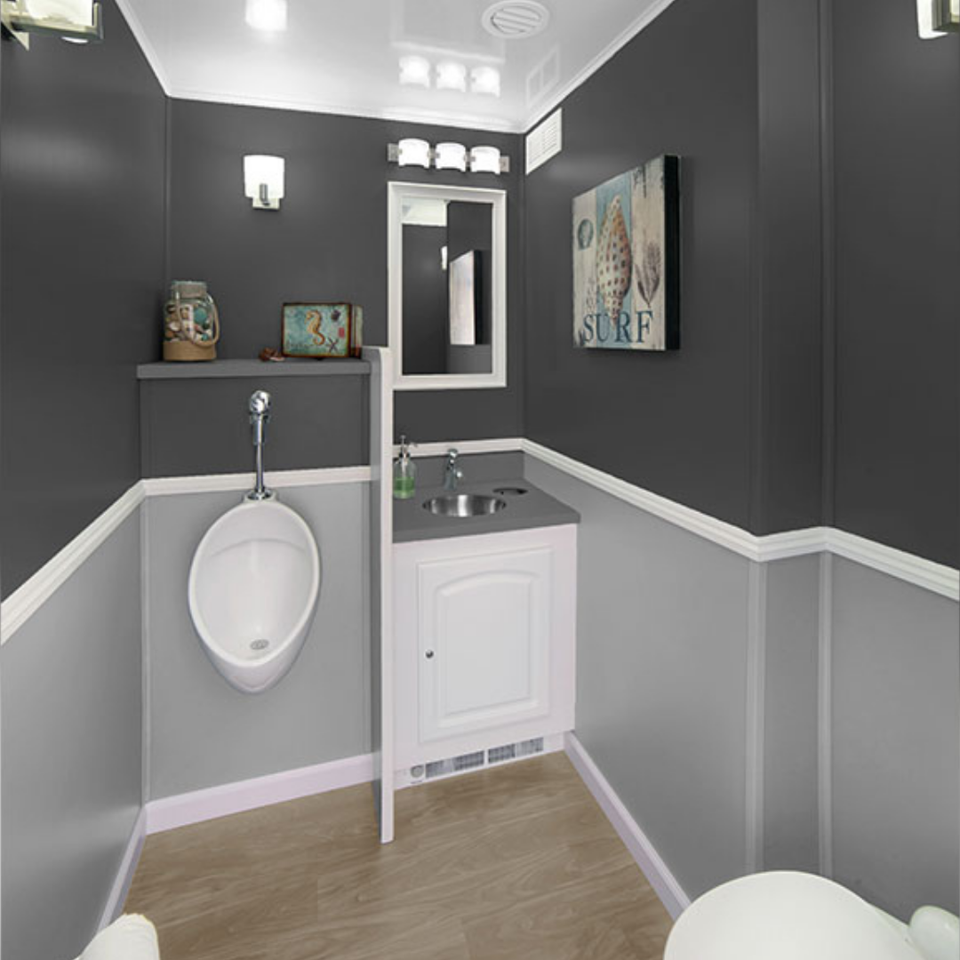 Small bathroom with dark gray upper walls and light gray lower walls, featuring a white urinal, sink with dark countertop, mirror, beach-themed decor, and light wood flooring.