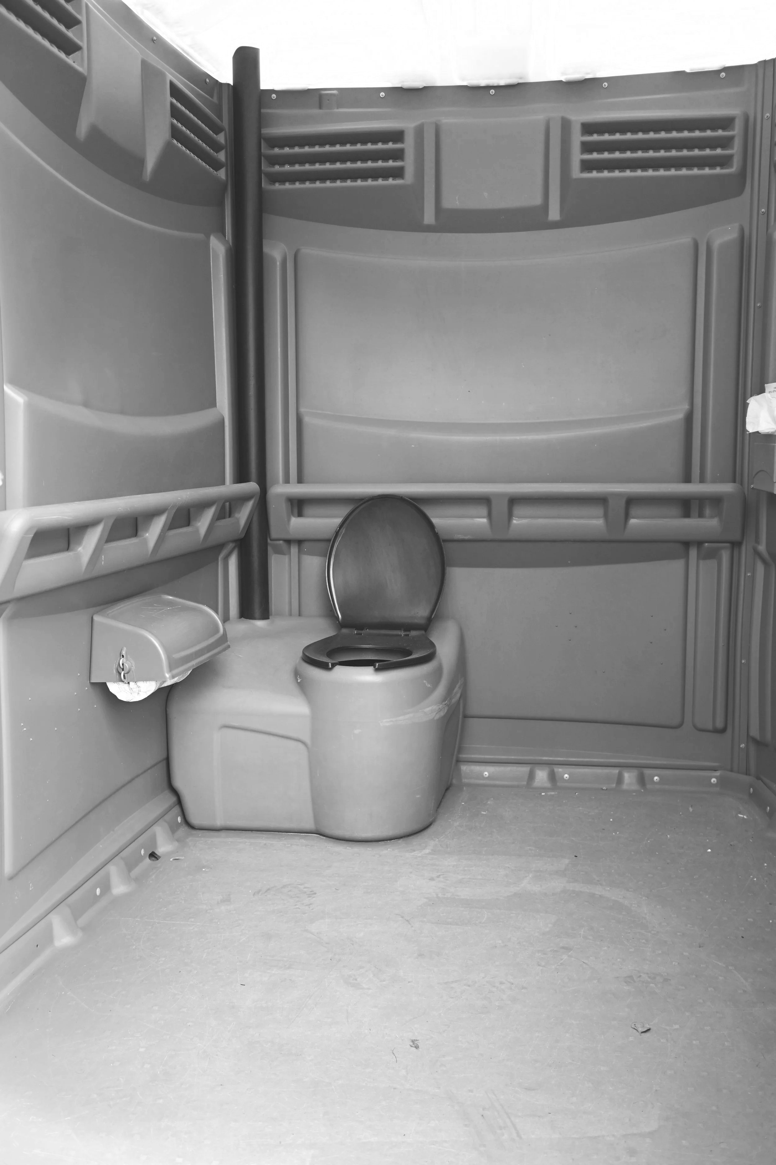 Inside a portable restroom, showing a toilet with the seat down, a small sink, and plastic shelves along the walls.