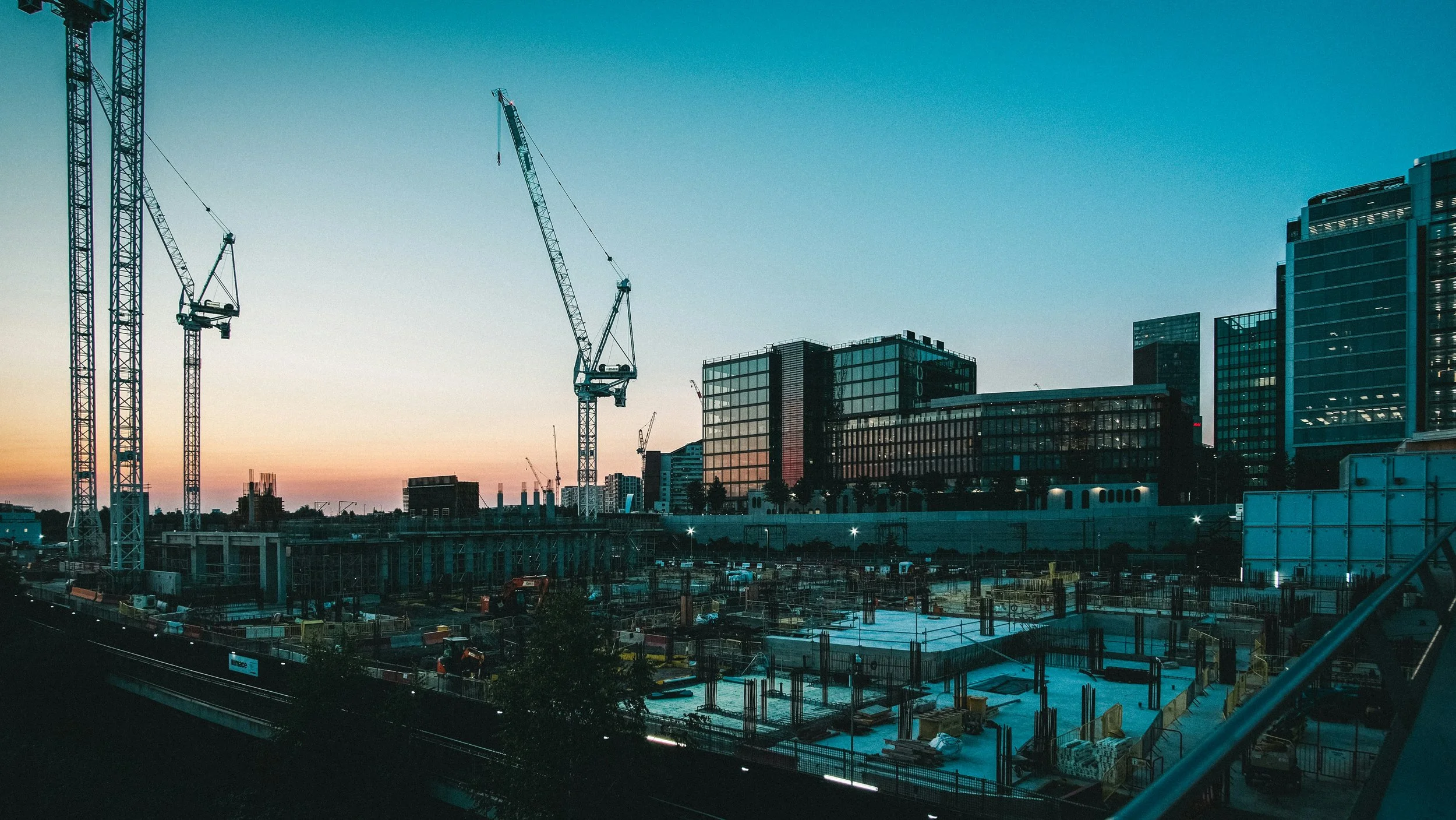 Construction site in a city with several high-rise buildings and cranes during sunset.