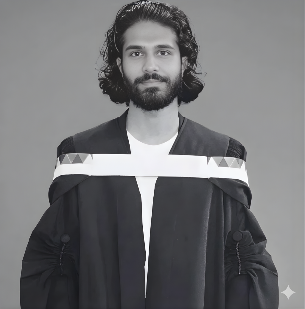 A young man with long, curly hair and a beard dressed in a graduation gown and hood, posing against a plain background.
