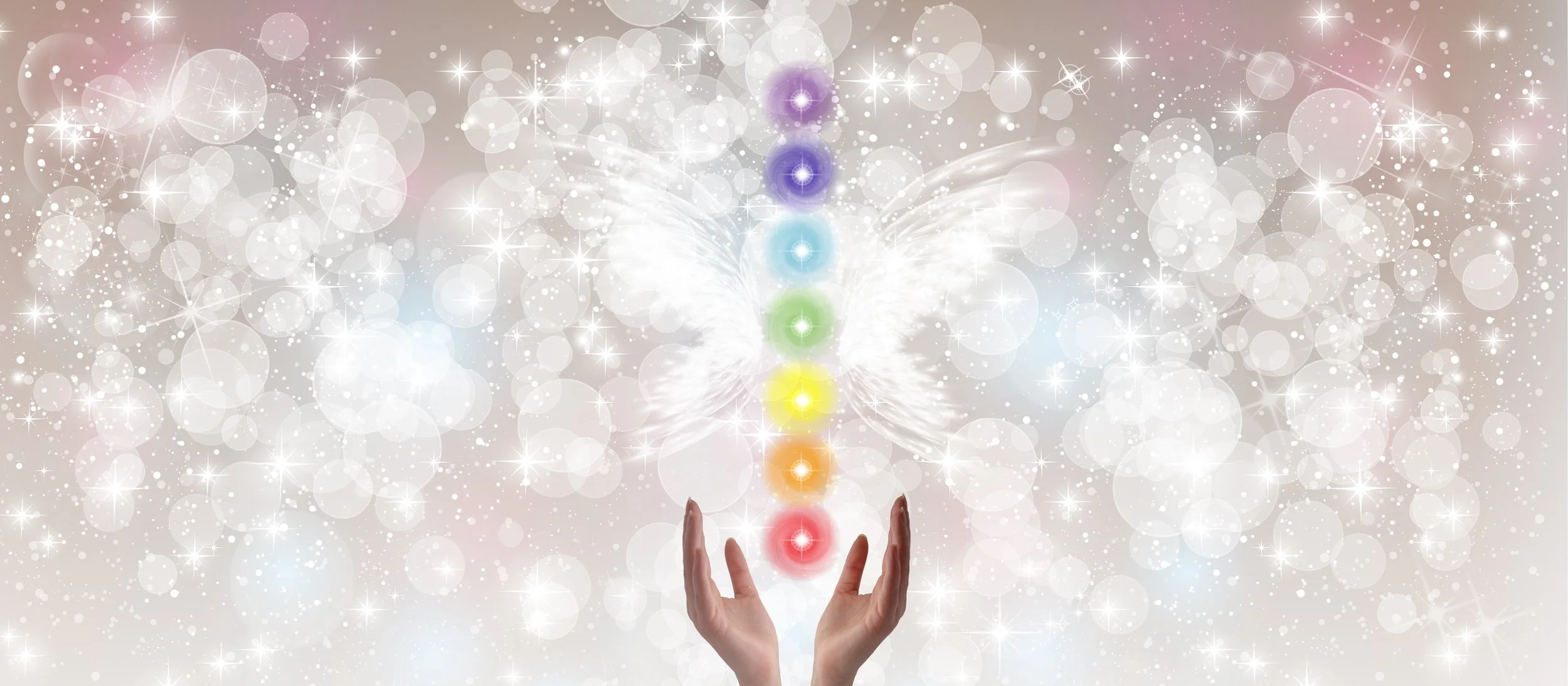 Hands reaching up towards a glowing, digital representation of the seven chakras with white butterfly wings and sparkling light effects in the background.