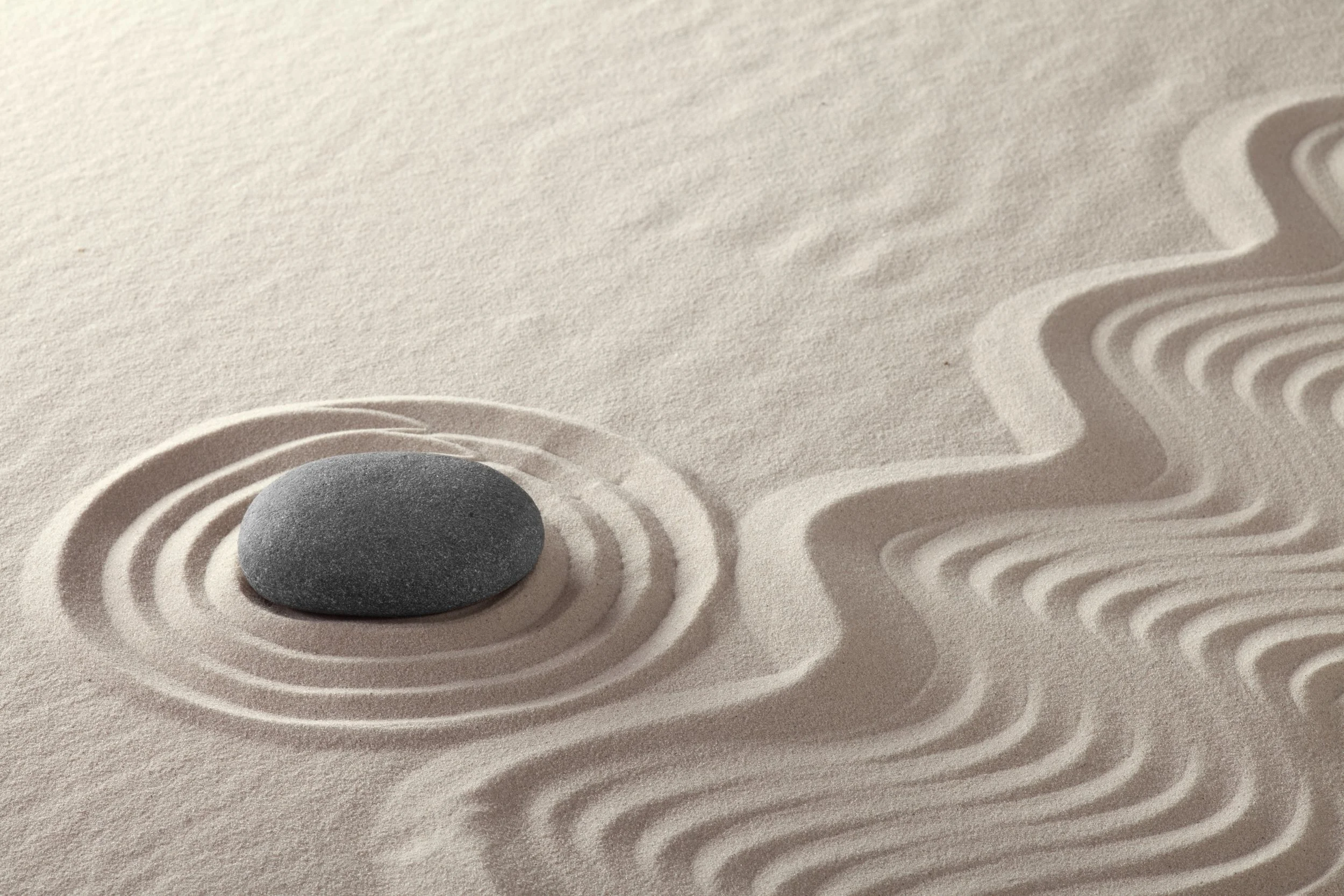 A smooth gray stone resting on sand with raked patterns around it.