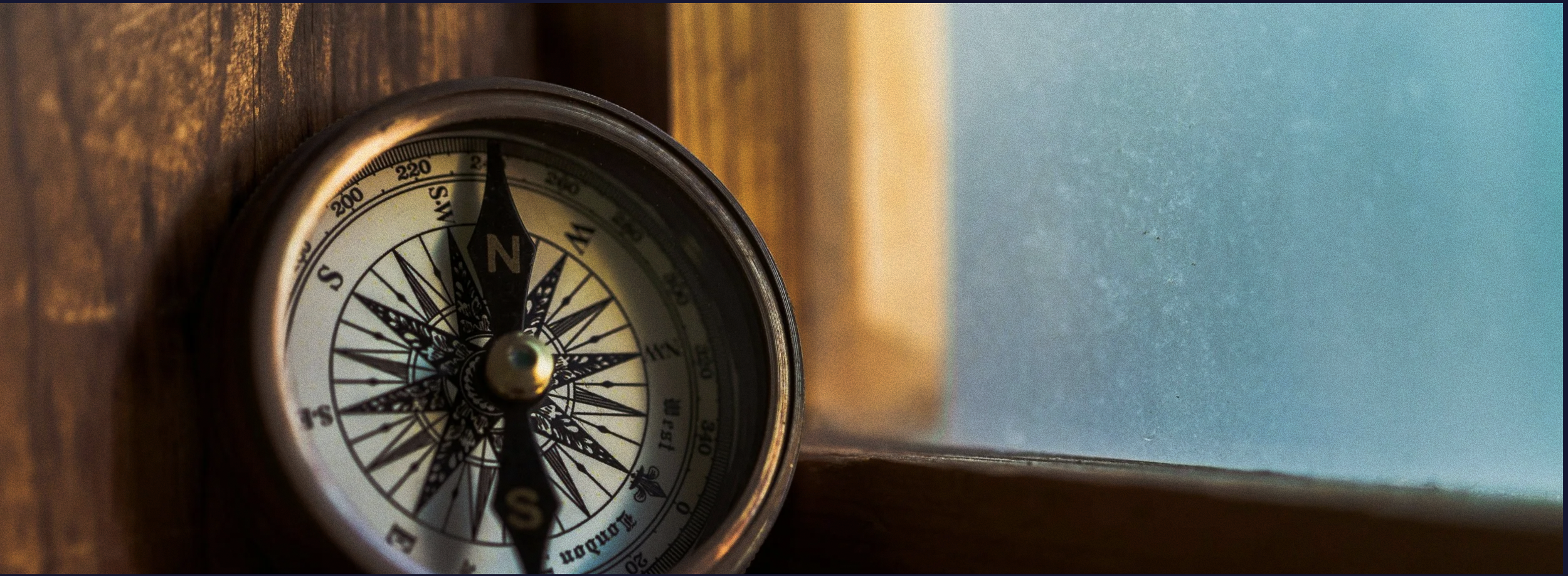 Close-up of a vintage compass with a black needle pointing north, placed on a wooden surface next to a blue wall.