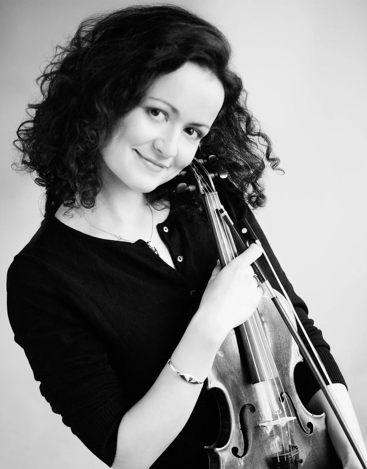 Black and white photo of a woman with curly hair holding a violin and bow, smiling.