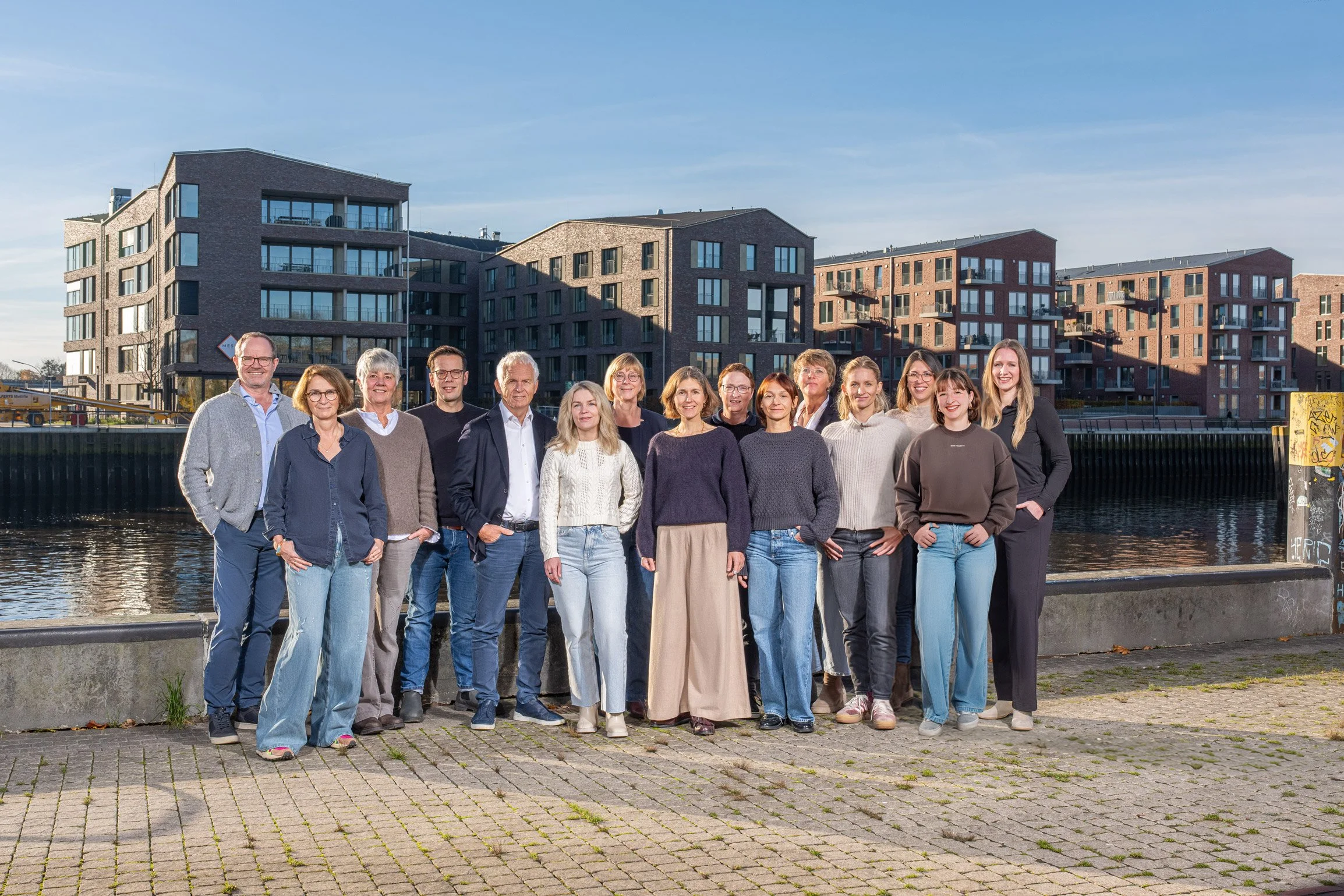 Gruppe von Menschen vor modernen Wohngebäuden am Wasser bei sonnigem Wetter.
