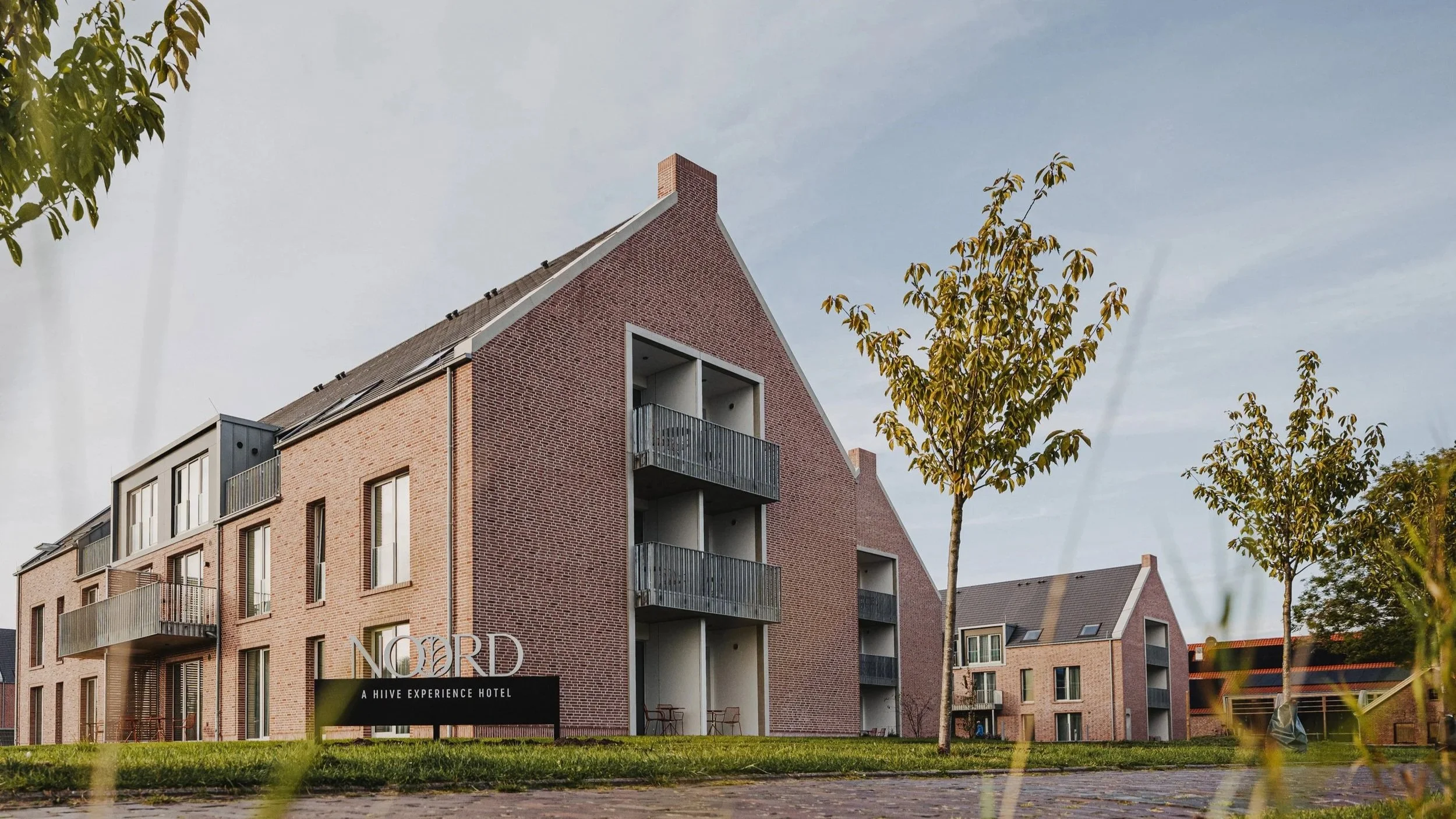 Moderne mehrstöckige Apartmenthäuser mit Balkonen, umgeben von Bäumen auf grünem Rasen, bei sonnigem Himmel.
