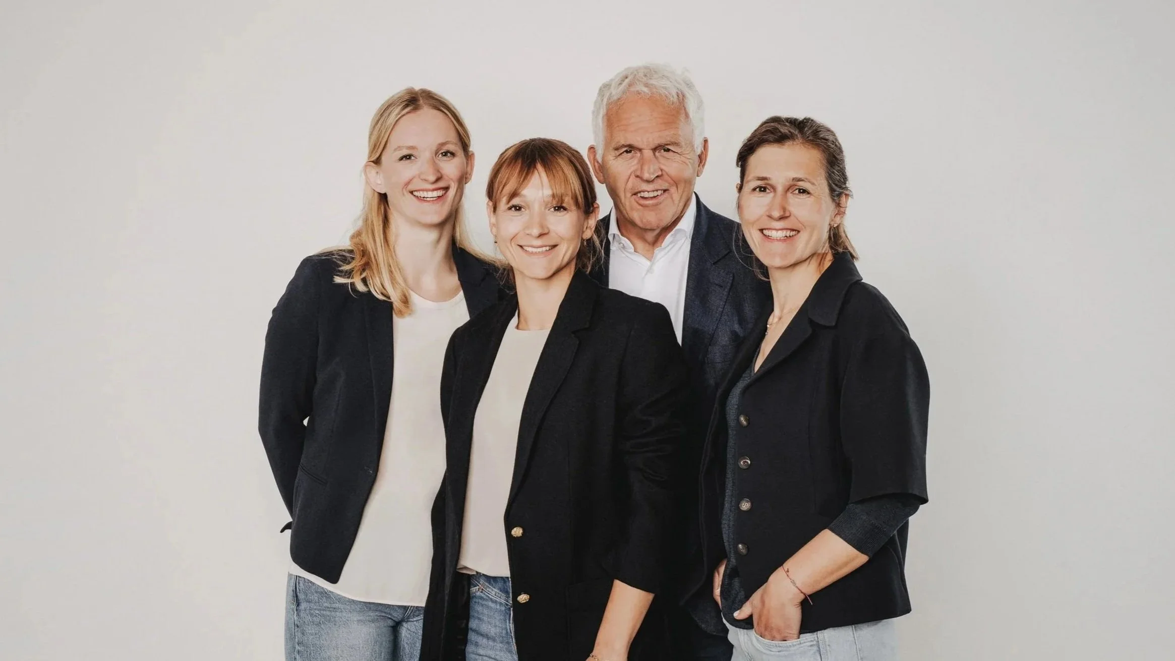 Vier lachende Menschen in professioneller Kleidung vor weißem Hintergrund.