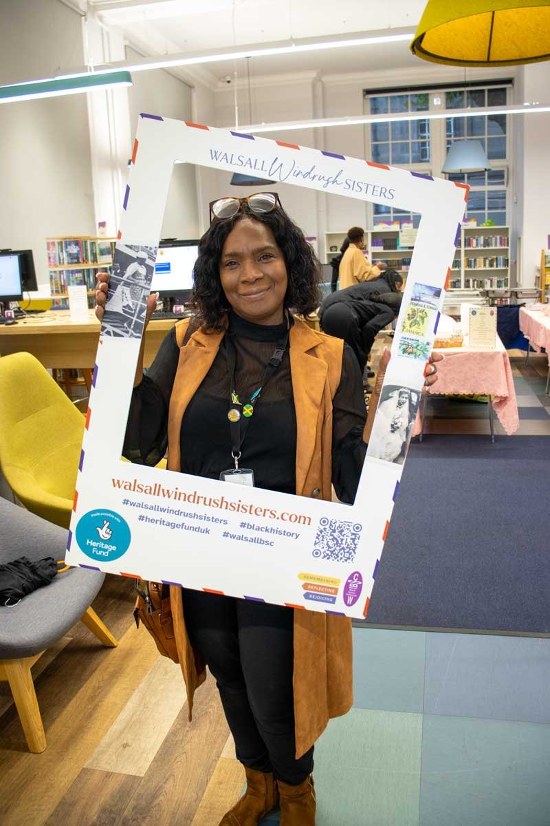 Smartly dressed black woman in a library holding up a selfie frame with her face framed in the middle