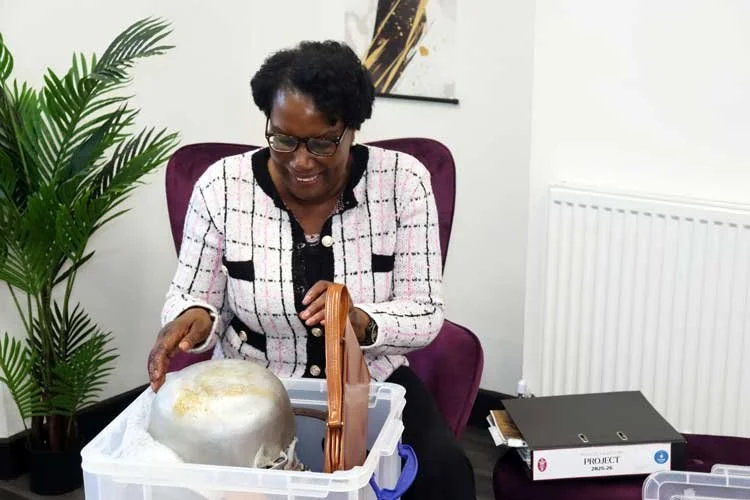 Mature black woman smiling into a storage box full of caribbean items like a dutchpot in an beautiful office