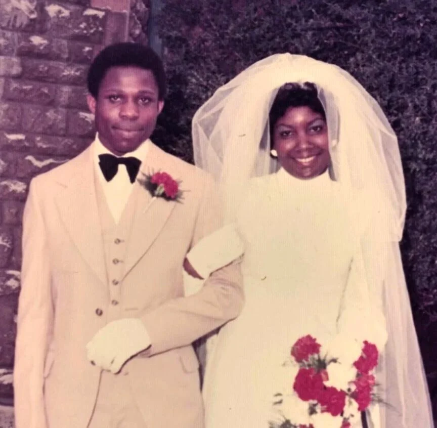 Lucille Paul and her husband photographed on their wedding day, the bride in a flowing white gown and veil holding a bouquet of red roses — a treasured family moment preserved within the Walsall Windrush Sisters Caribbean heritage archive.