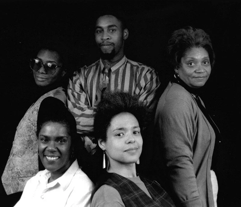 4 black women and a black man wearing stylish smart clothes grouped proudly together for a portrait