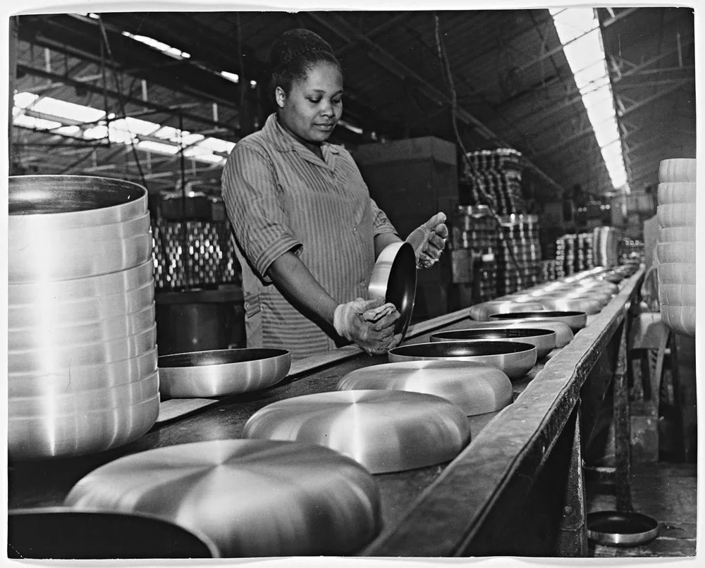 Black woman inspecting saucepans on an assembly line back in the 1960s