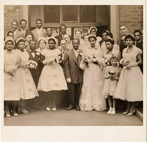 The large diverse wedding party of a glamorous young Jamaican couple gathered outside of the wedding venue in the 1950s