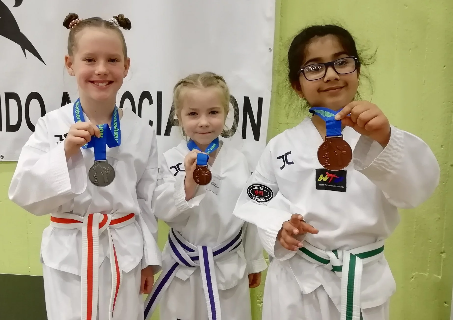 Three young girls in martial arts uniforms displaying medals on the podium.