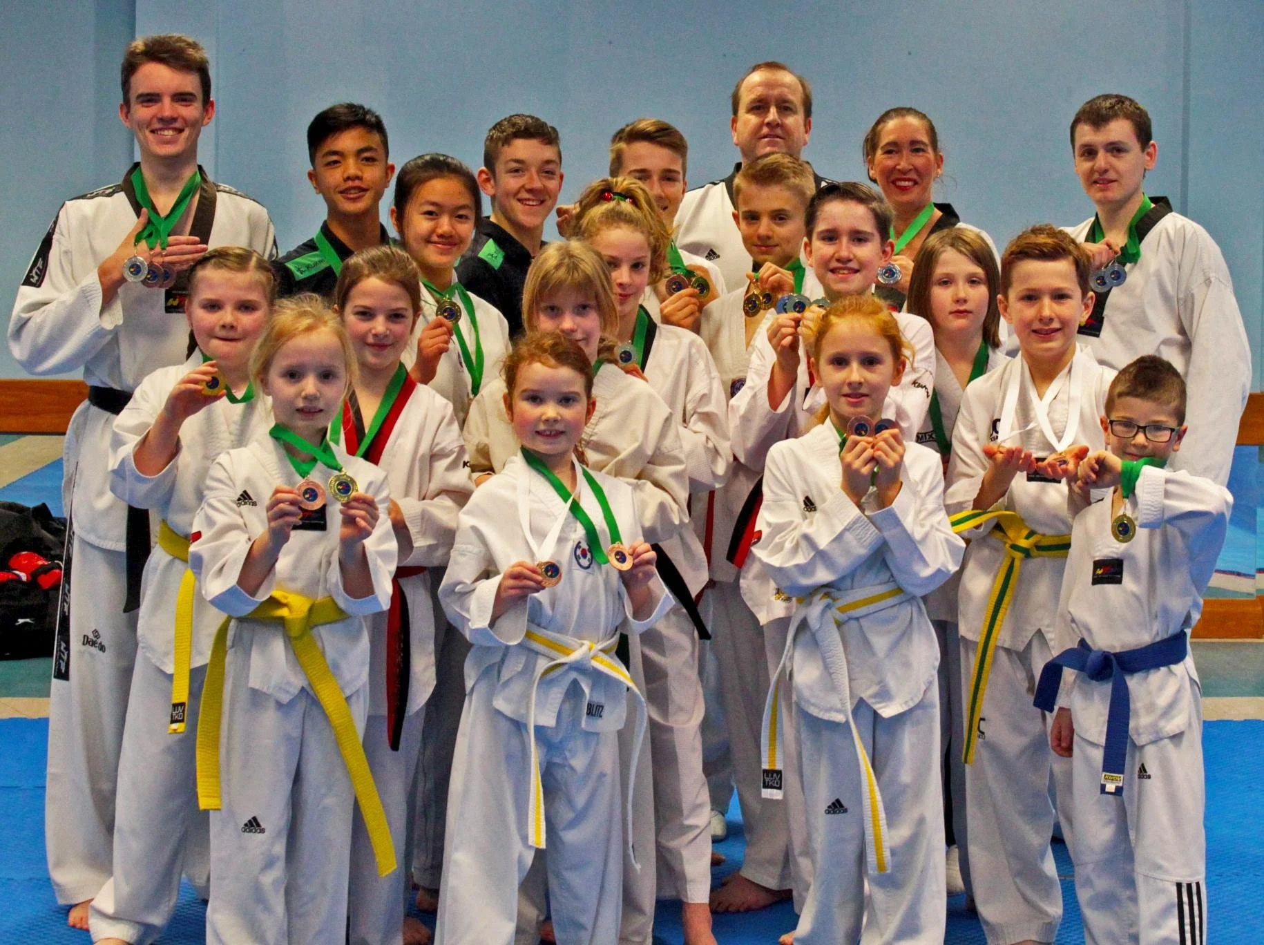 Group of children and adults in Taekwondo uniforms holding medals, celebrating a martial arts competition.