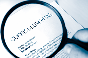 Close-up of a printed resume under a magnifying glass and a pen, with the heading 'CURRICULUM VITAE' visible.
