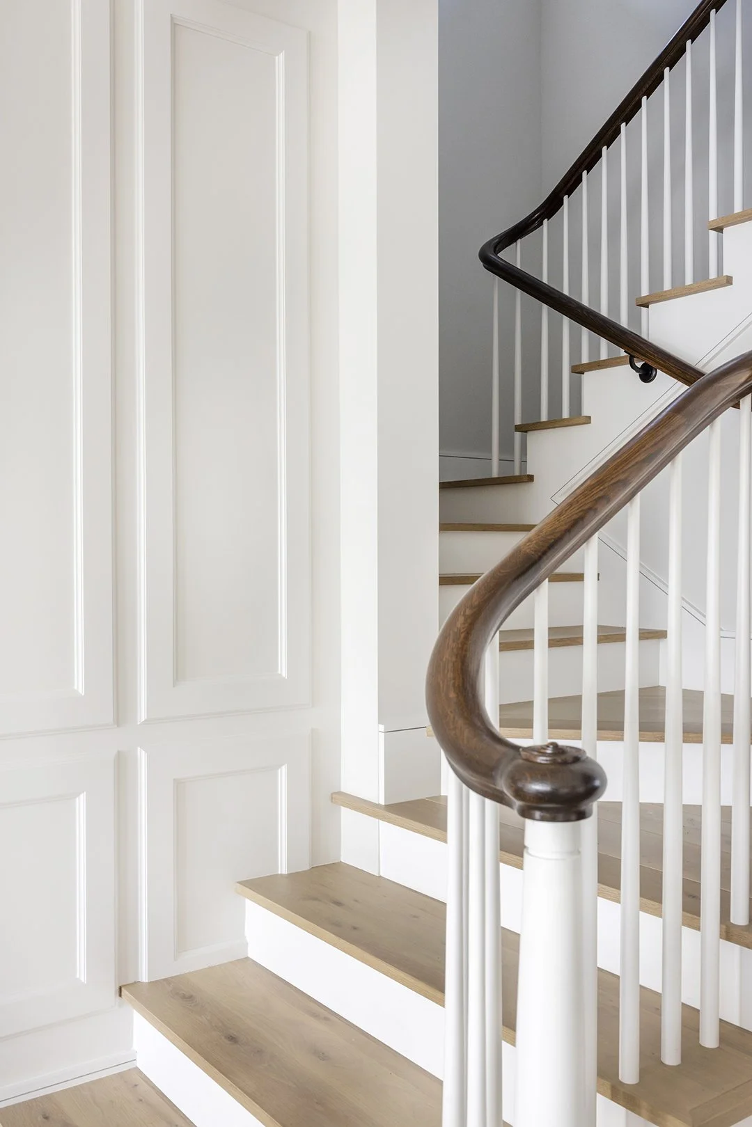 Interior view of a staircase with wooden handrails, white spindles, and light-colored wooden steps, beside a section of wall with a built-in closet.
