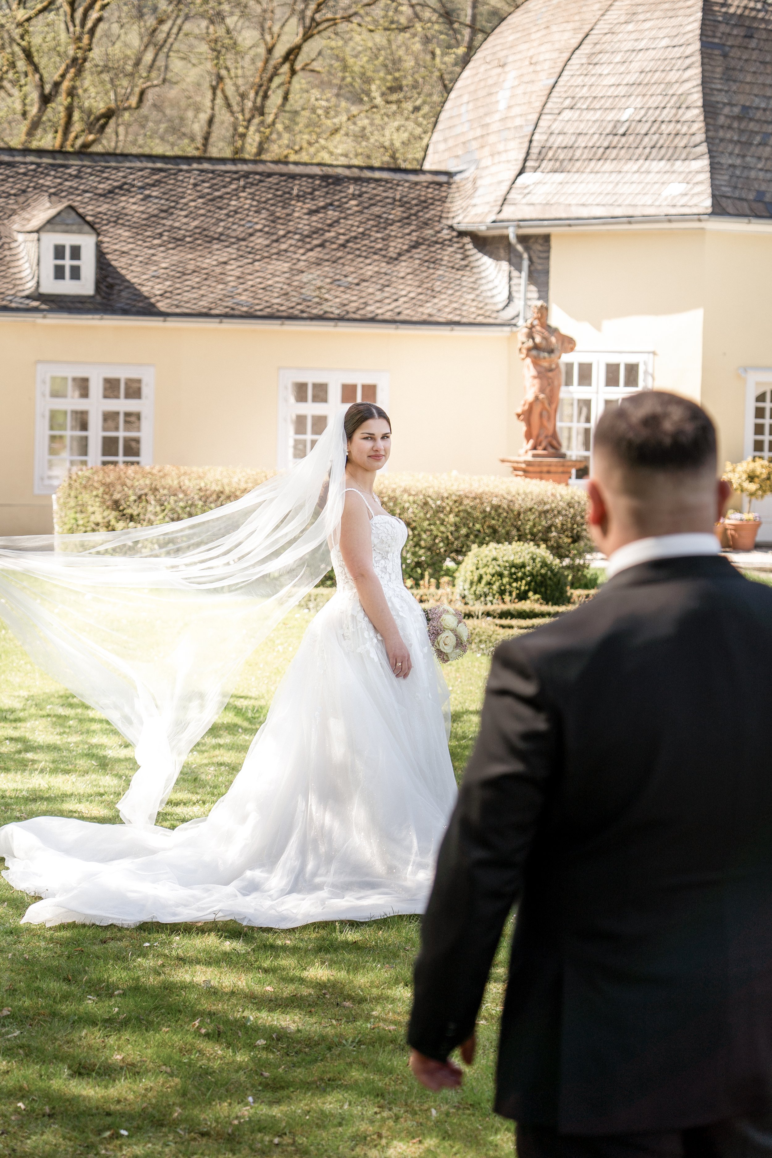 Braut und Bräutigam bei ihrer Hochzeit im Garten, mit einem Haus im Hintergrund und viel Sonnenschein.