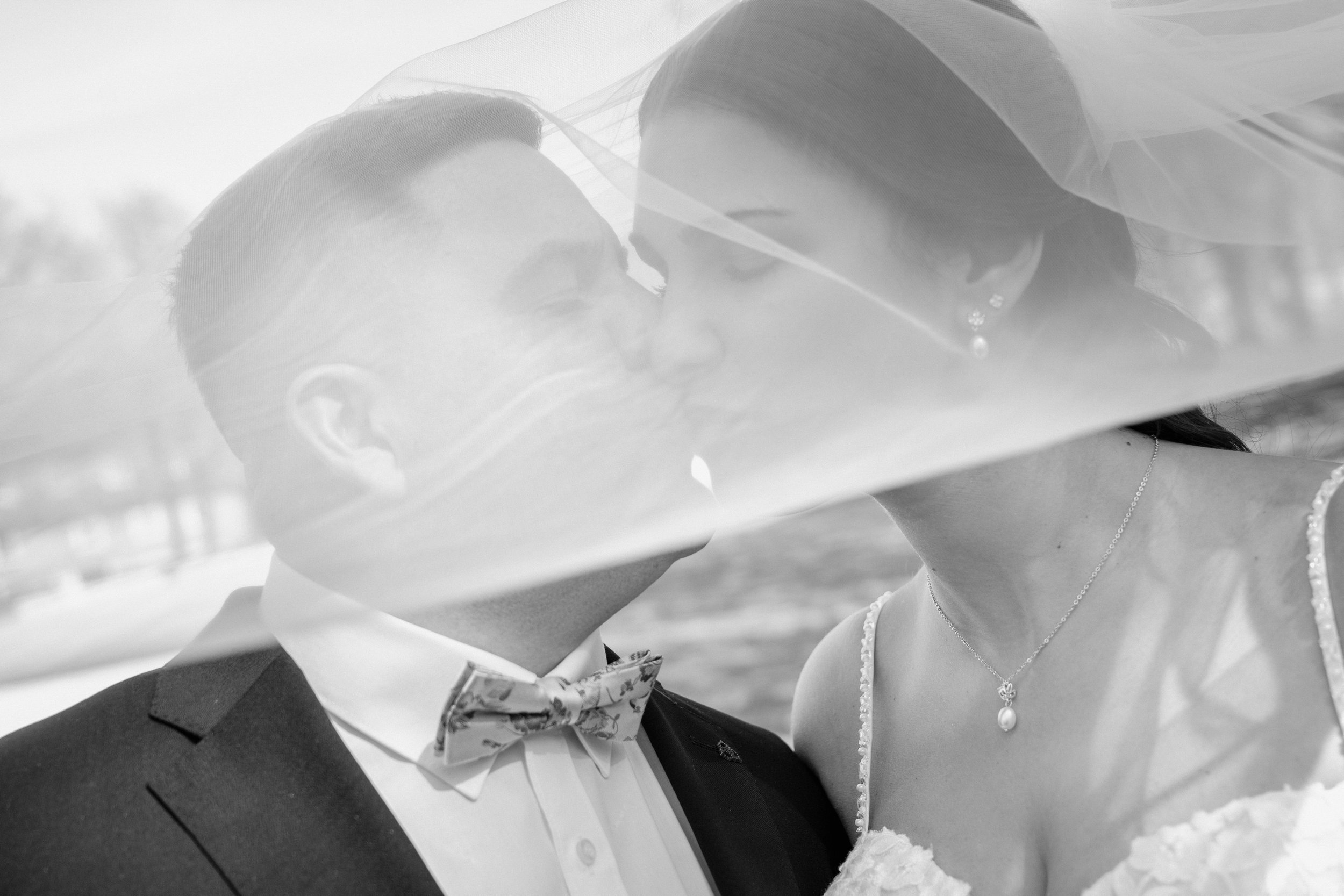 Ein Hochzeitsbild von einem Paar, das sich küsst, mit formeller Kleidung und Schmuck. Das Bild ist schwarz-weiß.