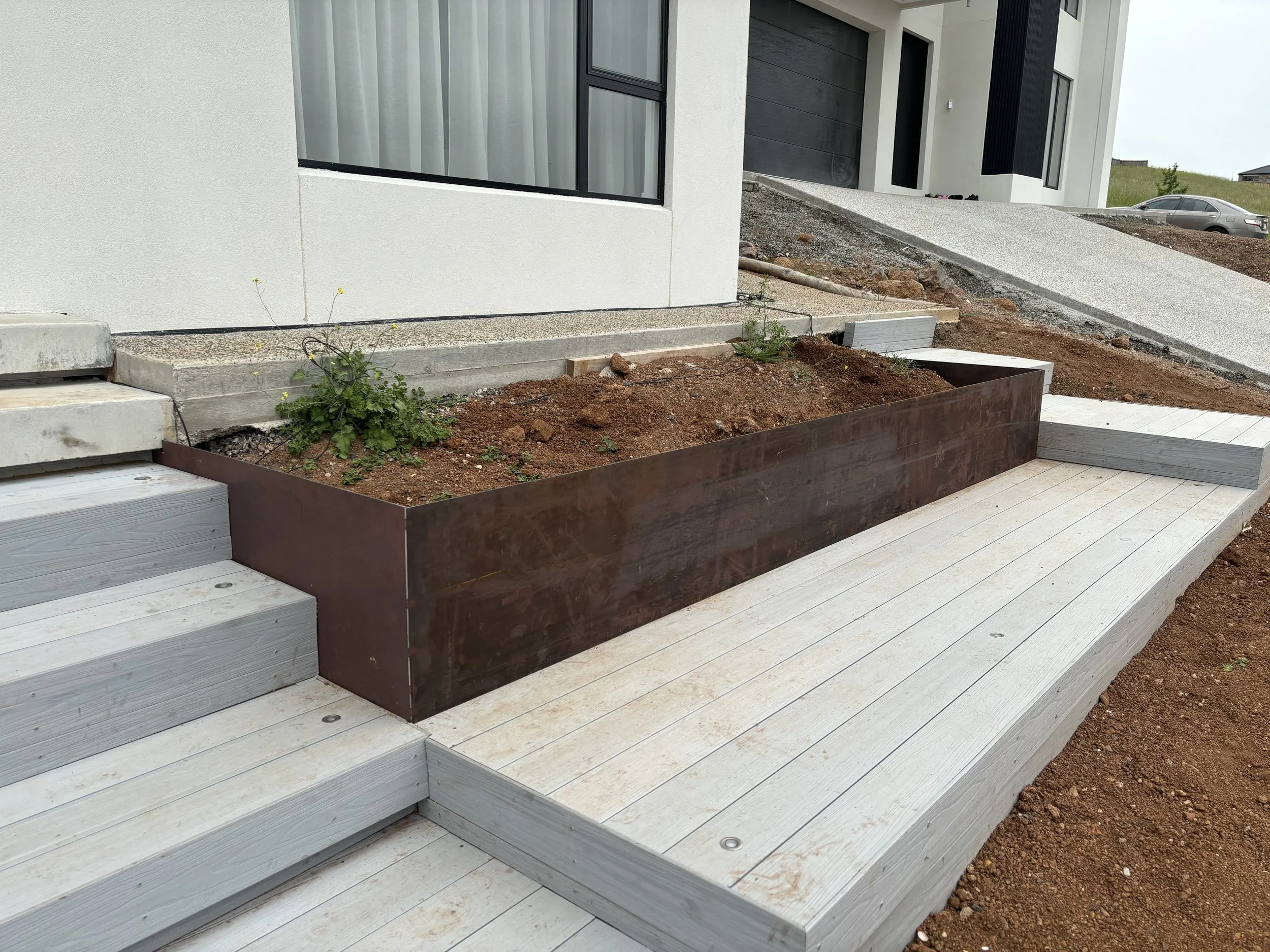 Newly constructed outdoor area with wooden decking, a corten metal planter box with growing plants
